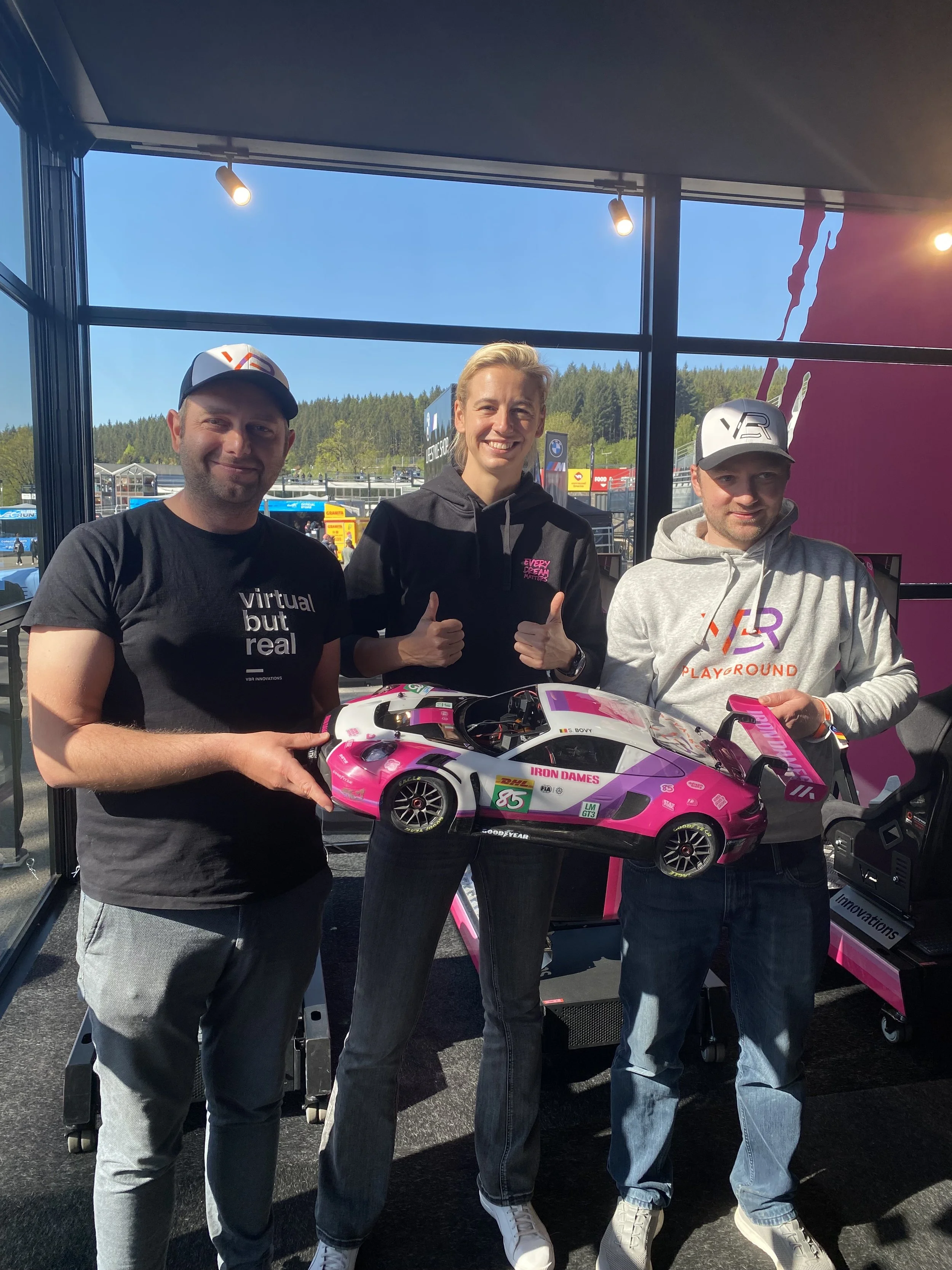 Crowd of people at an indoor event with colorful lighting, some standing near tech displays and a large green sign that says 'PLAY' and 'ROCK'.