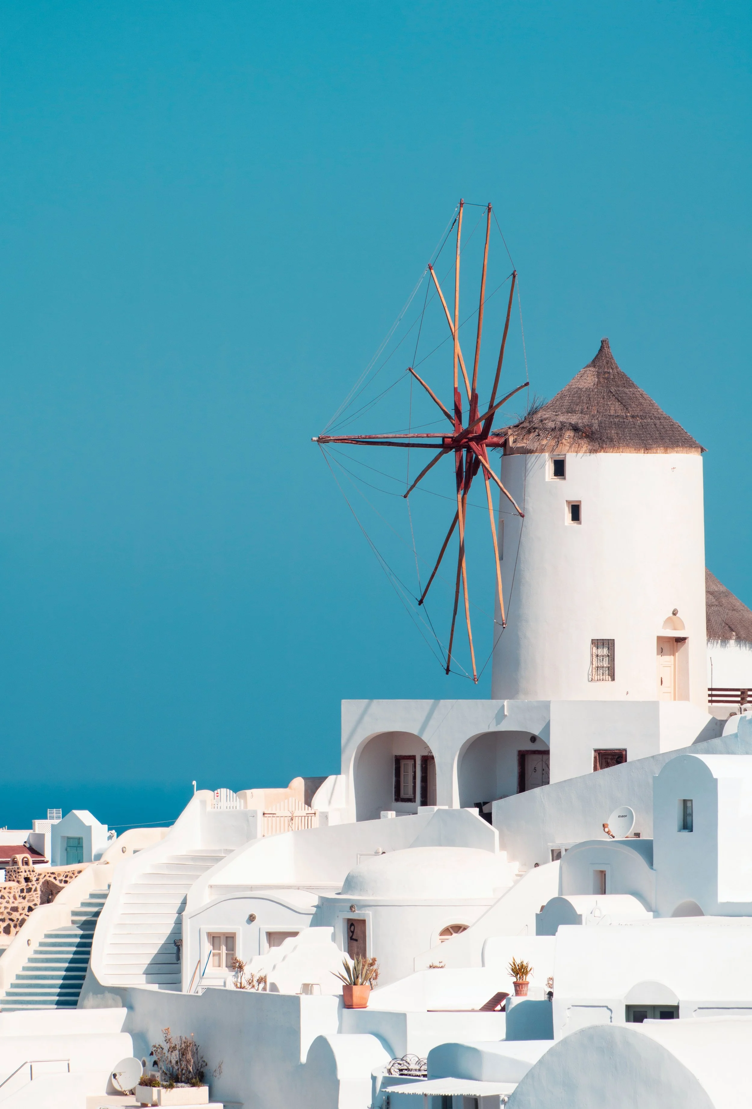 White buildings with curved roofs and a traditional windmill against a bright blue sky.