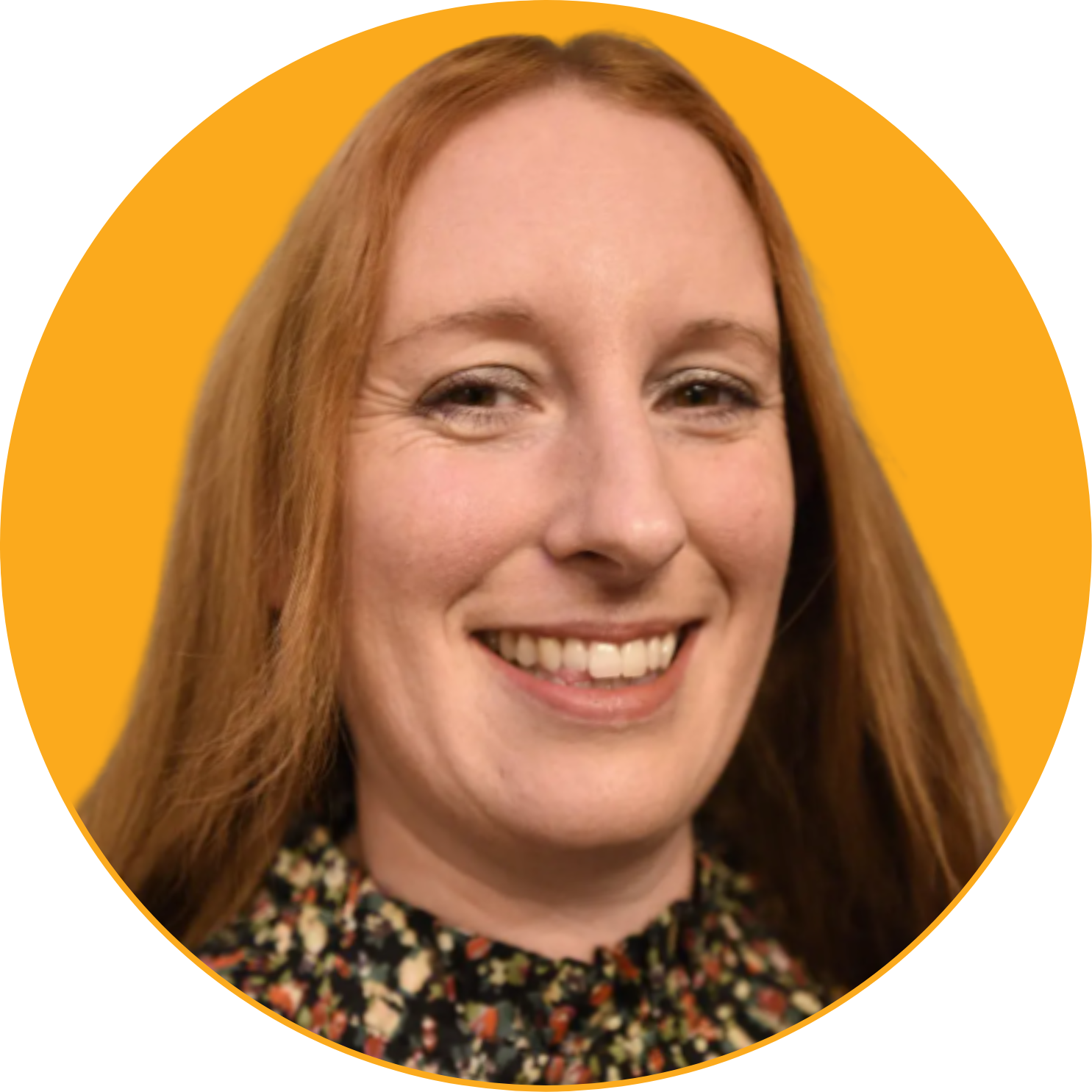 Close-up of a smiling woman with long red hair, wearing a black floral top, against a yellow background.