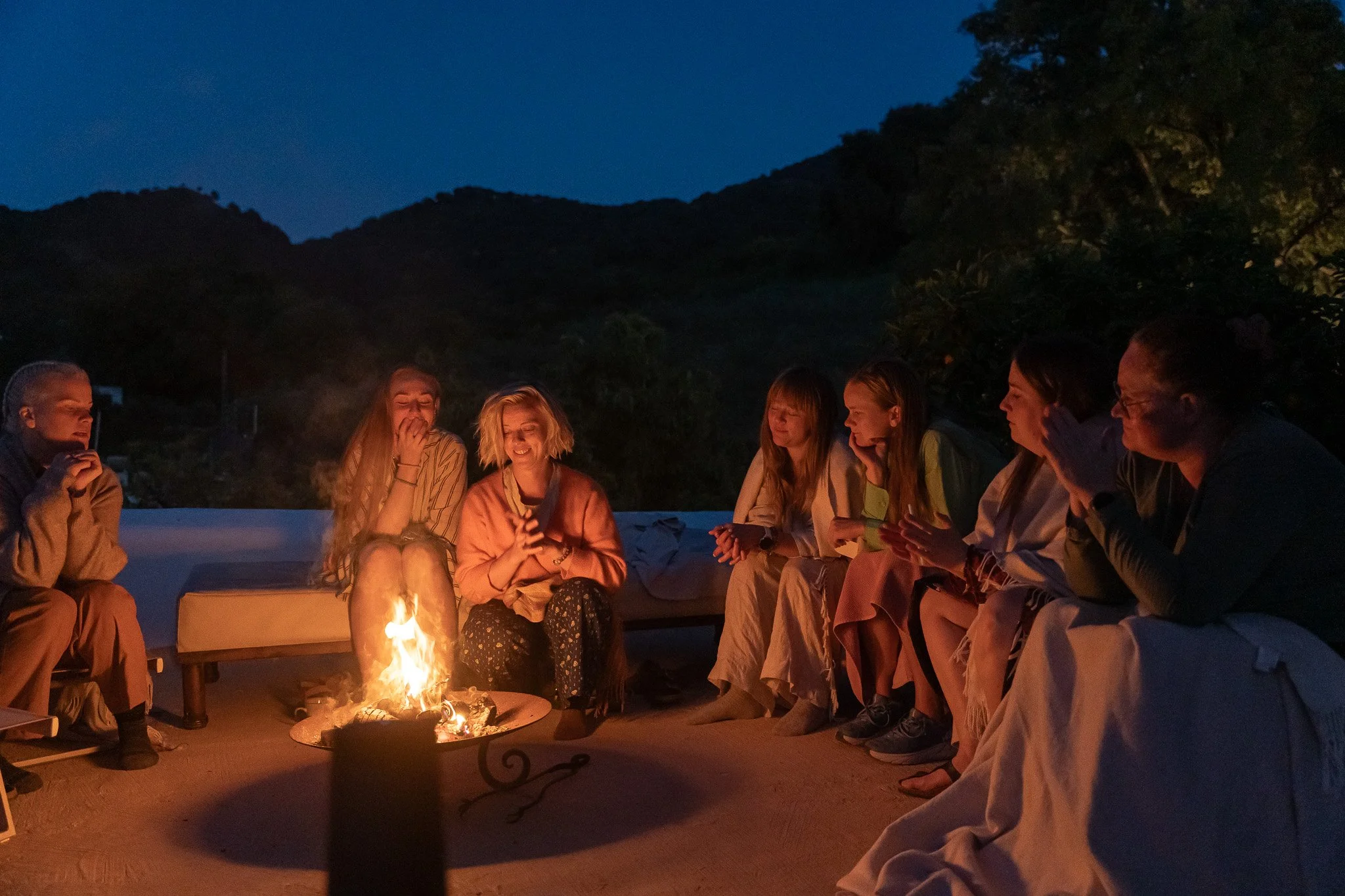 Kvinner på yoga-retreat sitter rundt et bål under stjernehimmelen