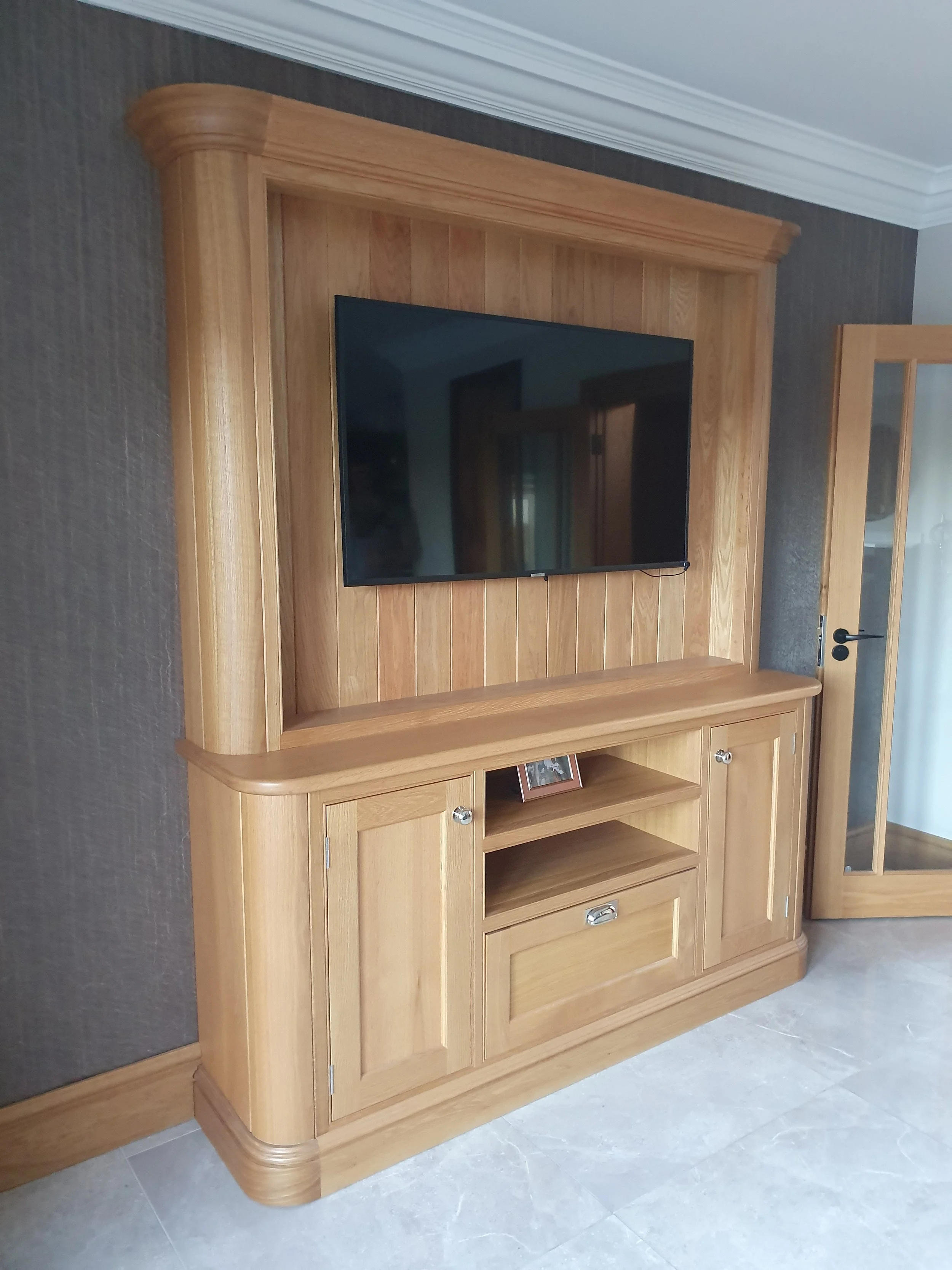 Wooden entertainment center with a mounted flat-screen TV and a framed photo on the shelf.