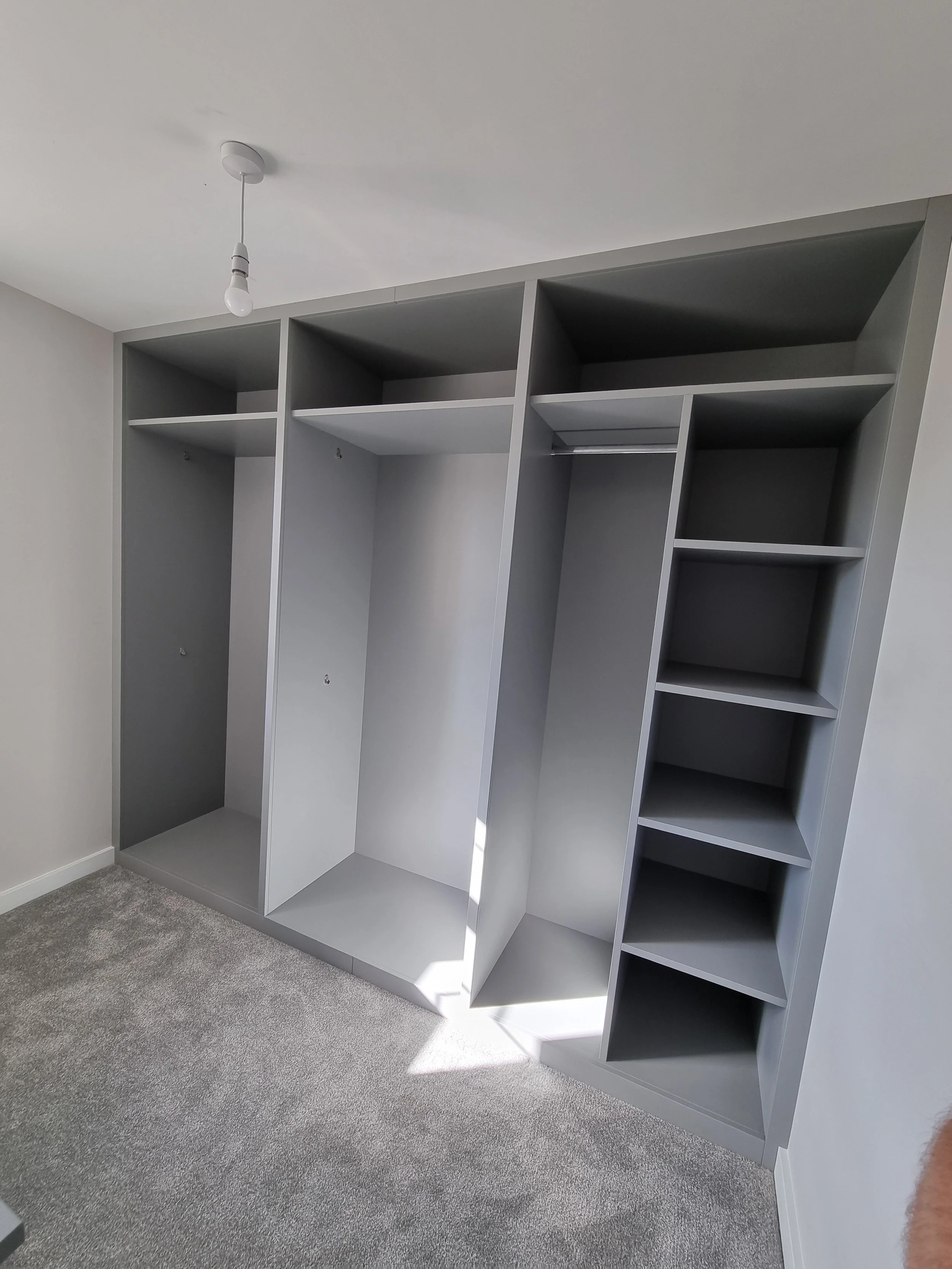 Empty gray wardrobe with open shelves and hanging compartments in a room with gray carpet and white walls.