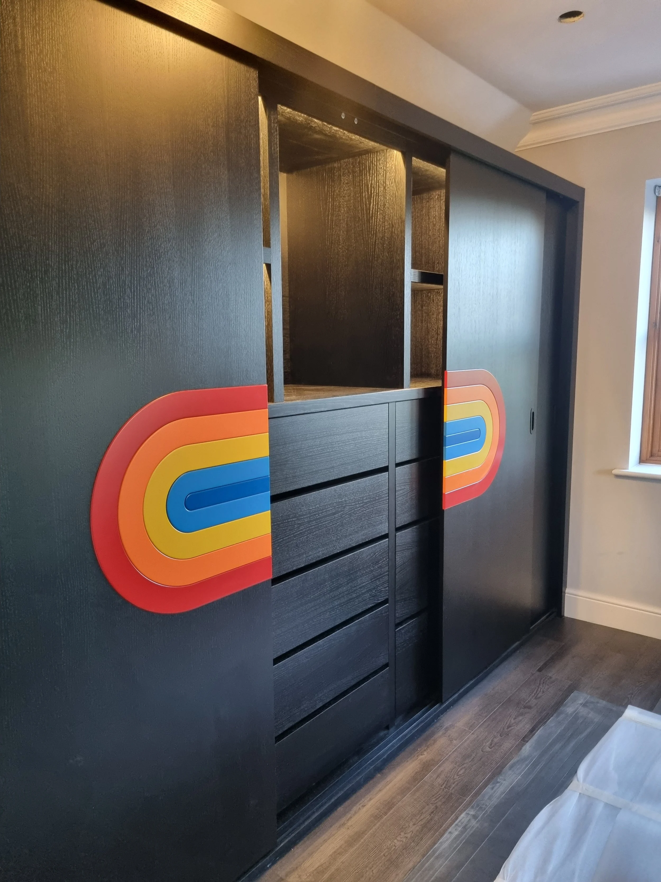 Black cabinet with colorful rainbow-shaped handles, reserved for displaying items, with drawers below.
