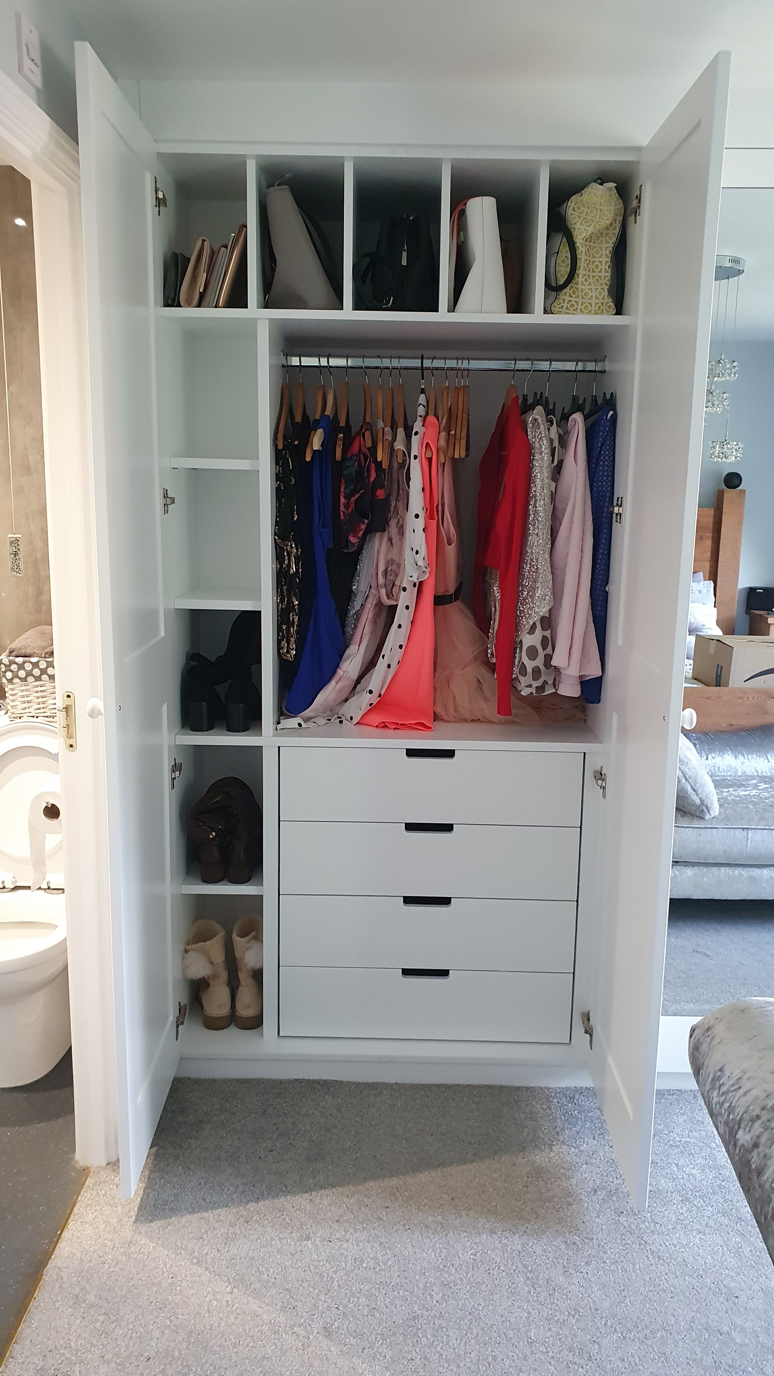 Open white wardrobe with clothes hanging, shoes and boots on shelves, and handbags on top shelf.