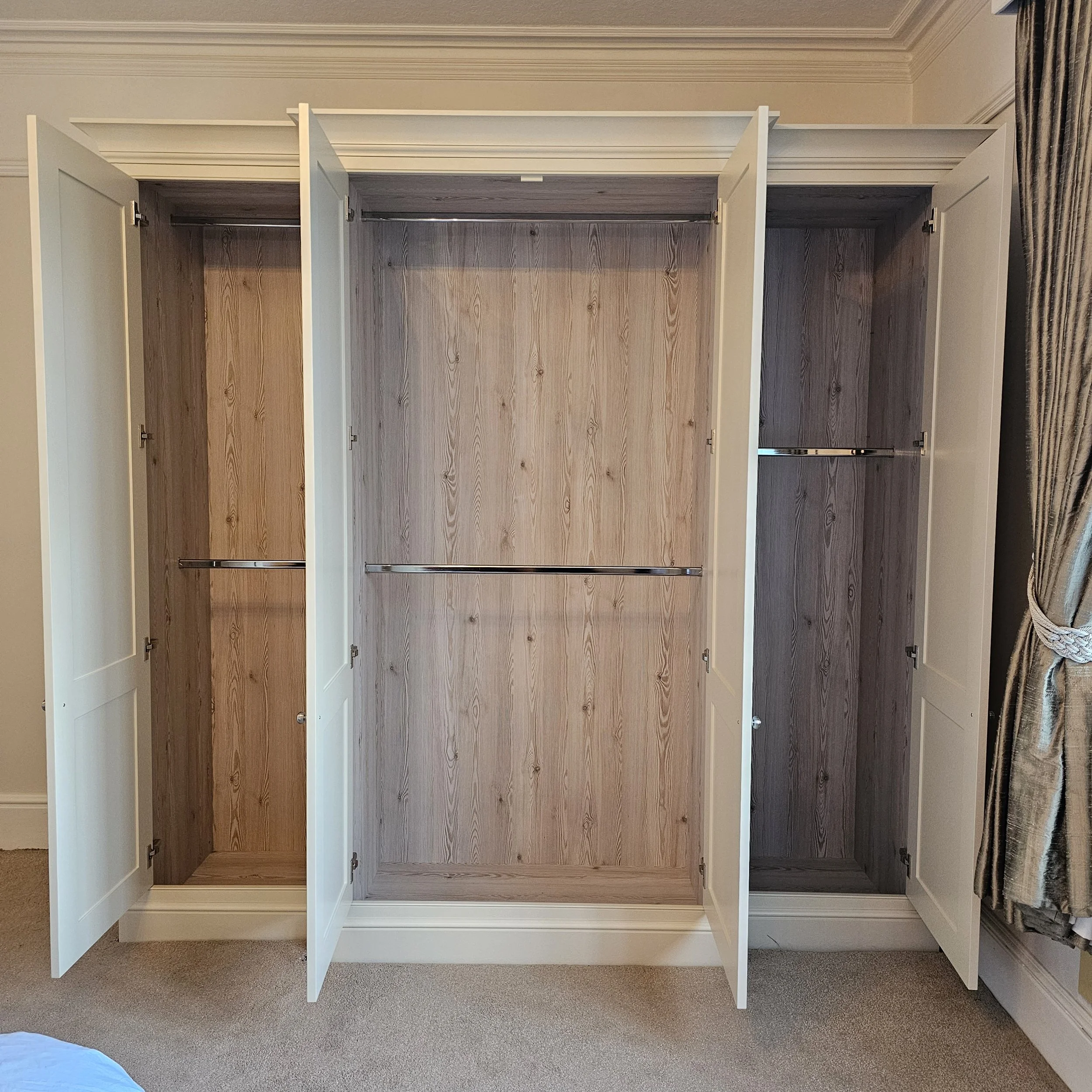 Empty built-in wardrobe with three sections, interior wood finish, and hanging rods.