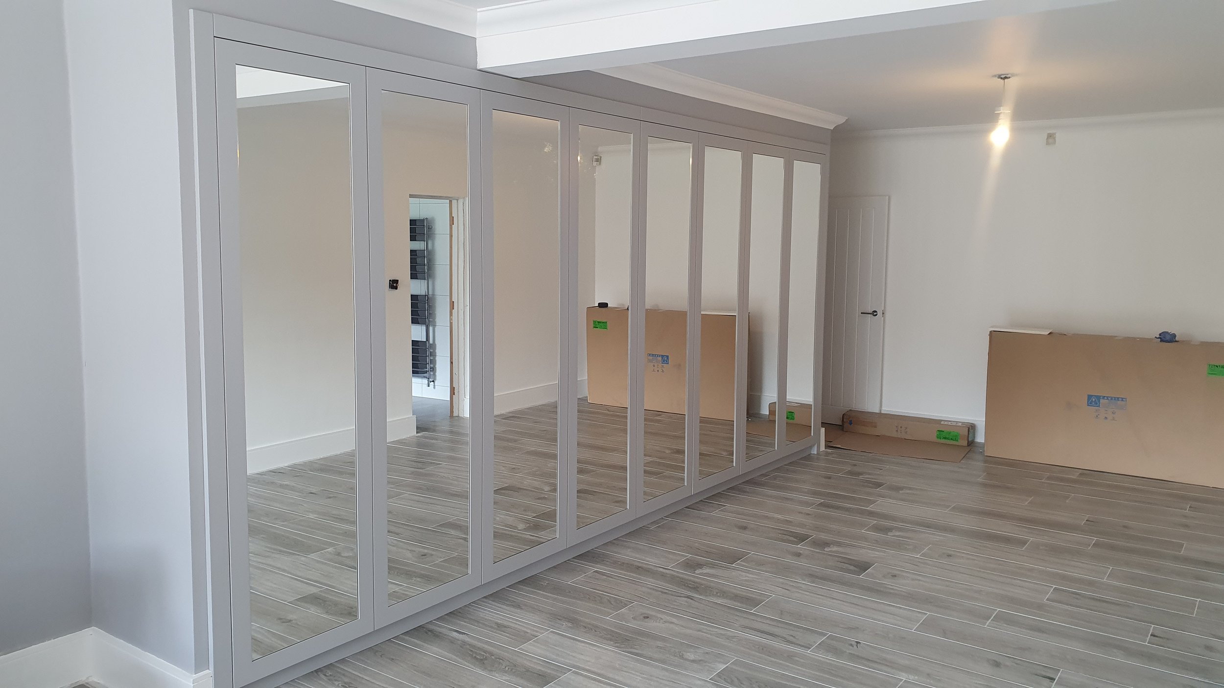 Interior of a room under renovation with a large mirror wall and cardboard boxes on the floor.