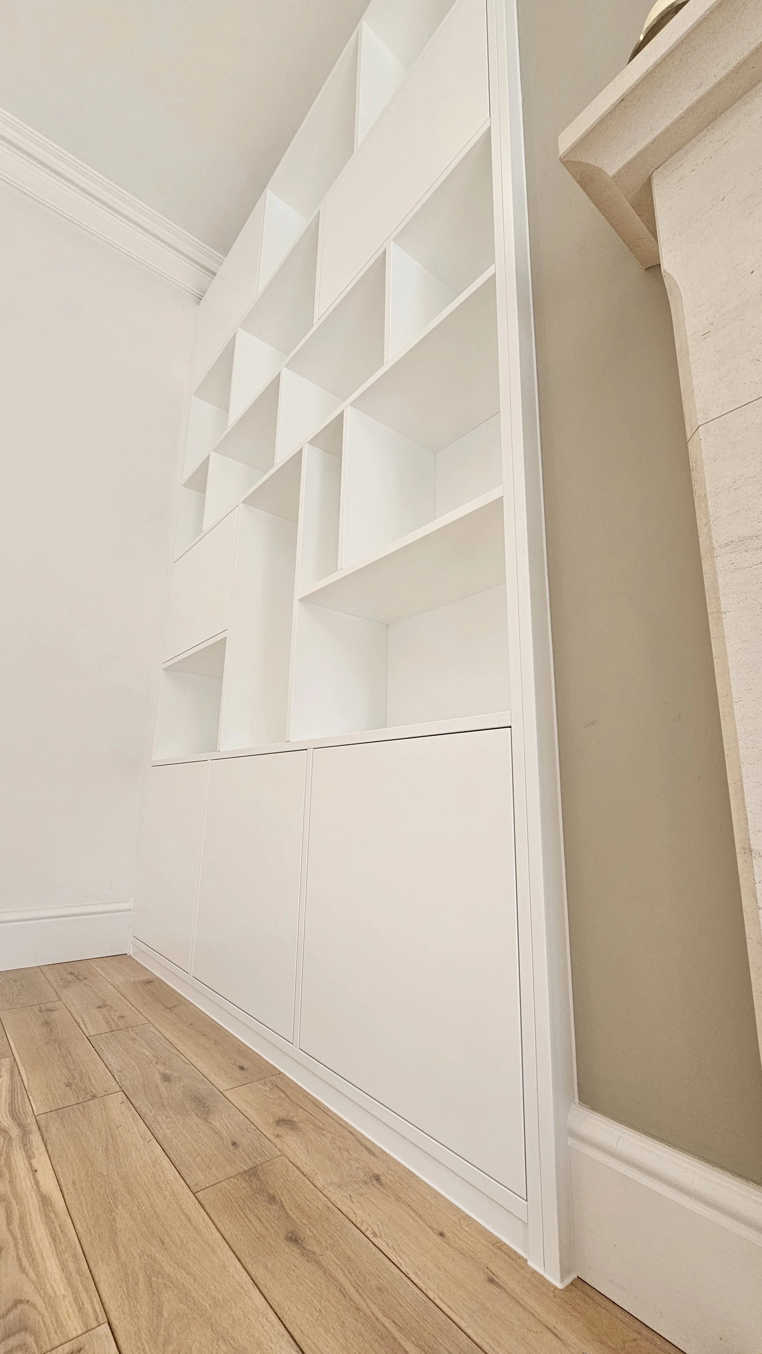 White storage unit with open shelves at the top and closed cabinets at the bottom, placed against a wall with a beige countertop nearby, in a home interior.