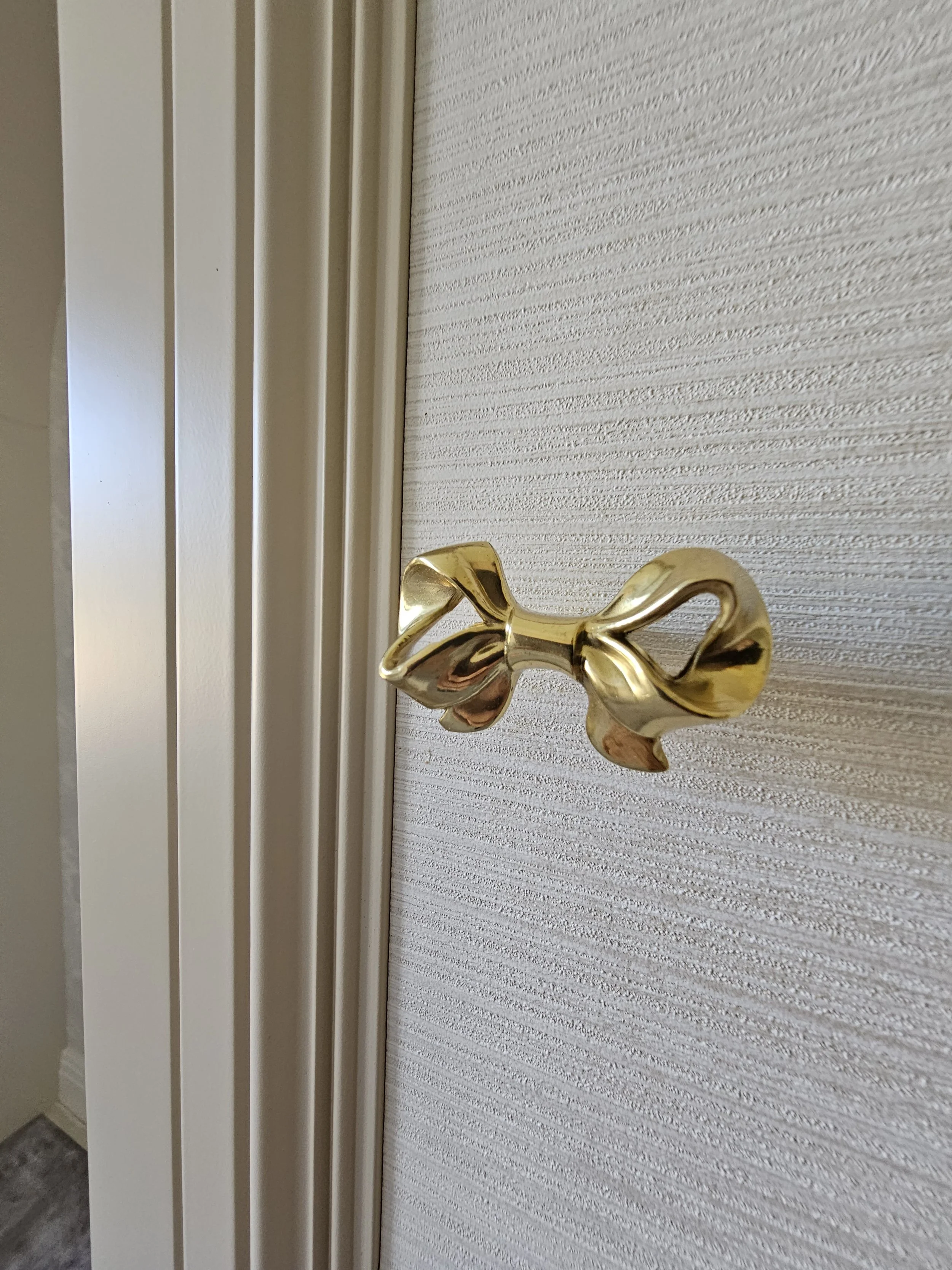 Close-up of a gold-colored decorative door knob on a textured, light-colored door.
