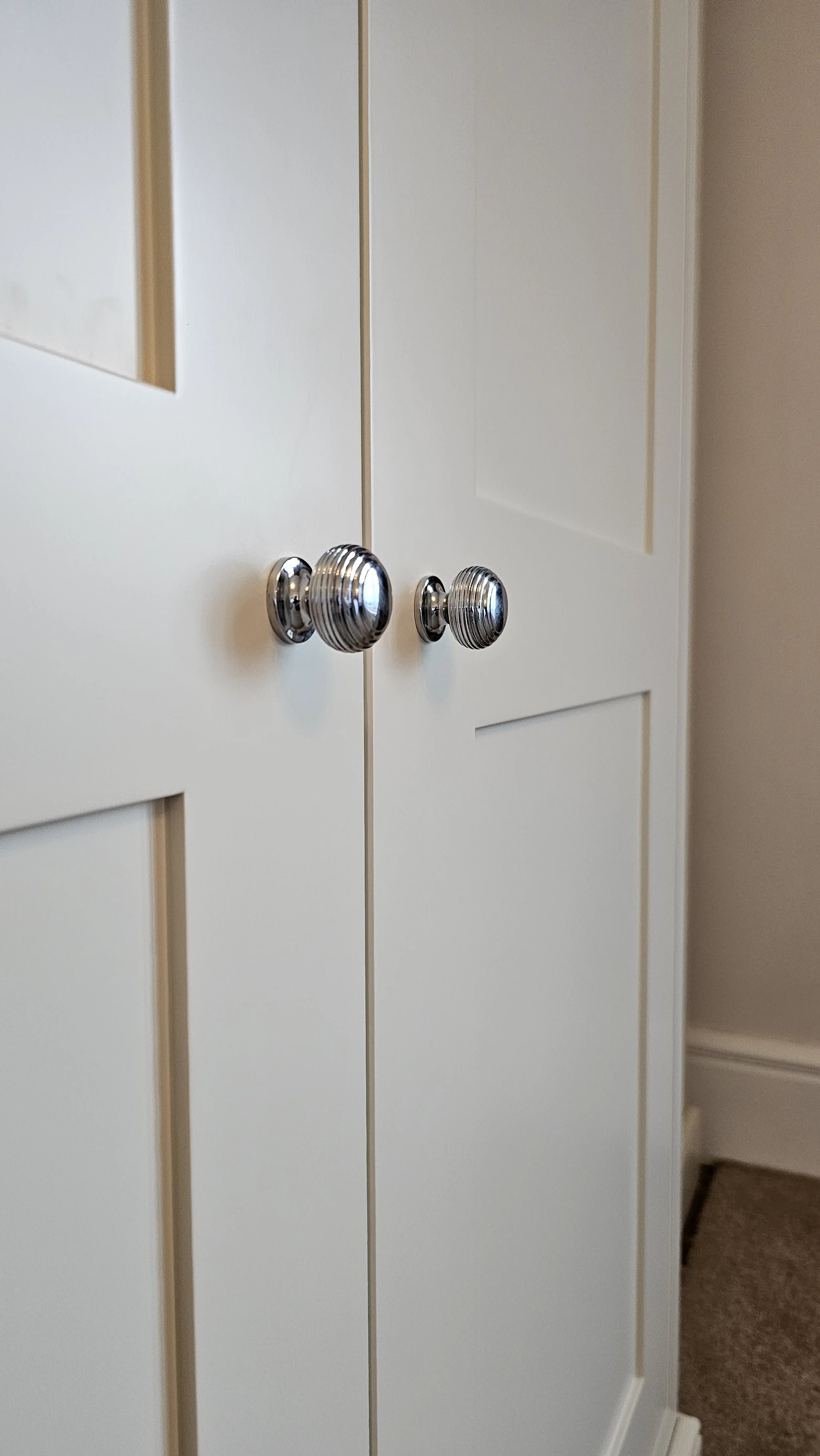 A close-up of cream-colored cabinet doors with silver, ribbed, round knobs in a home interior.