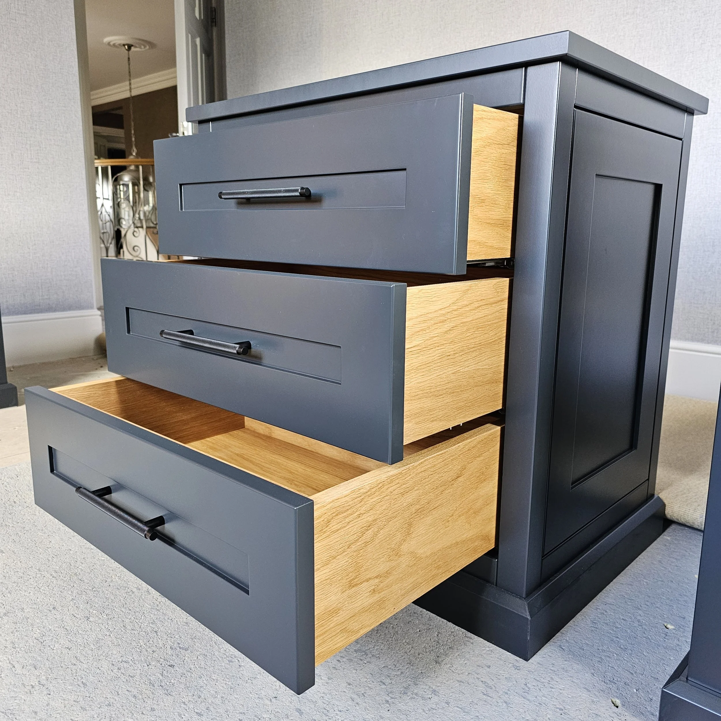 A dark blue wooden dresser with three drawers partially open, revealing light wood interiors, in a room with gray carpet and neutral walls.