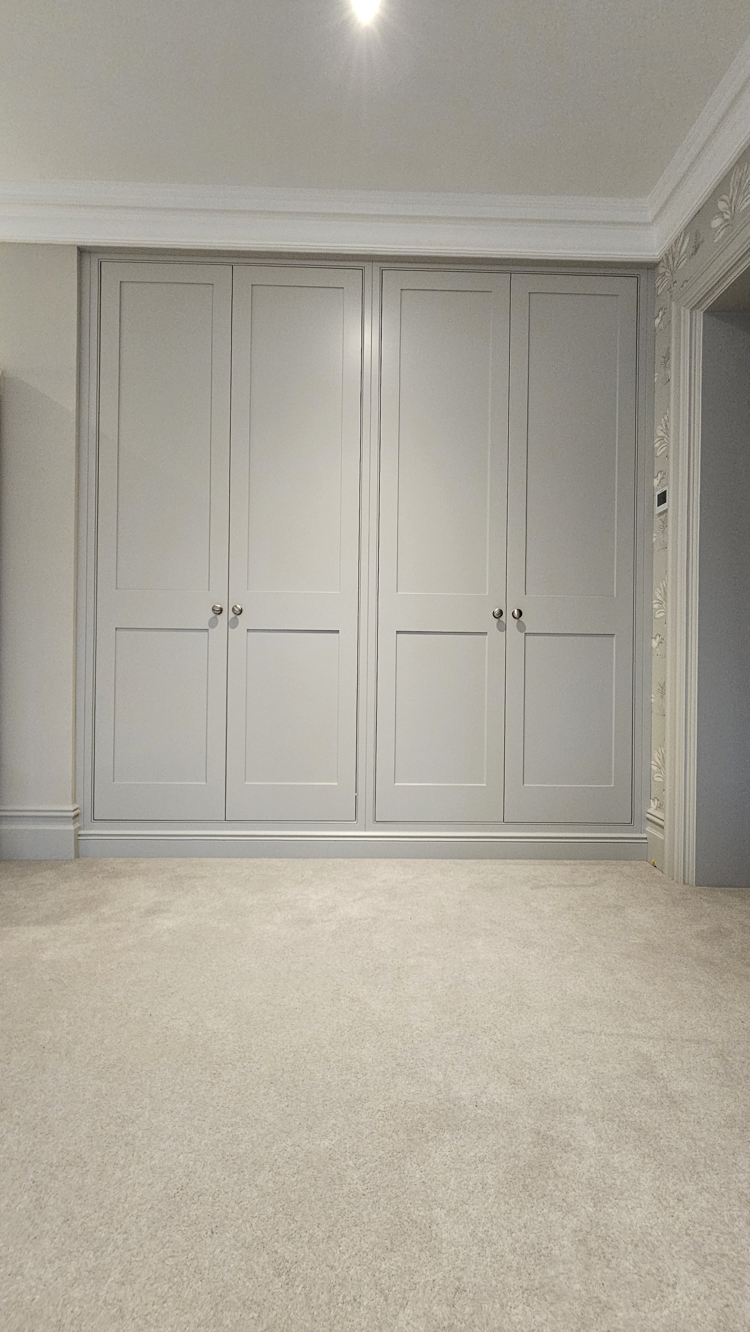 A large built-in closet with four closed doors in a painted white room with crown molding and a beige carpet.