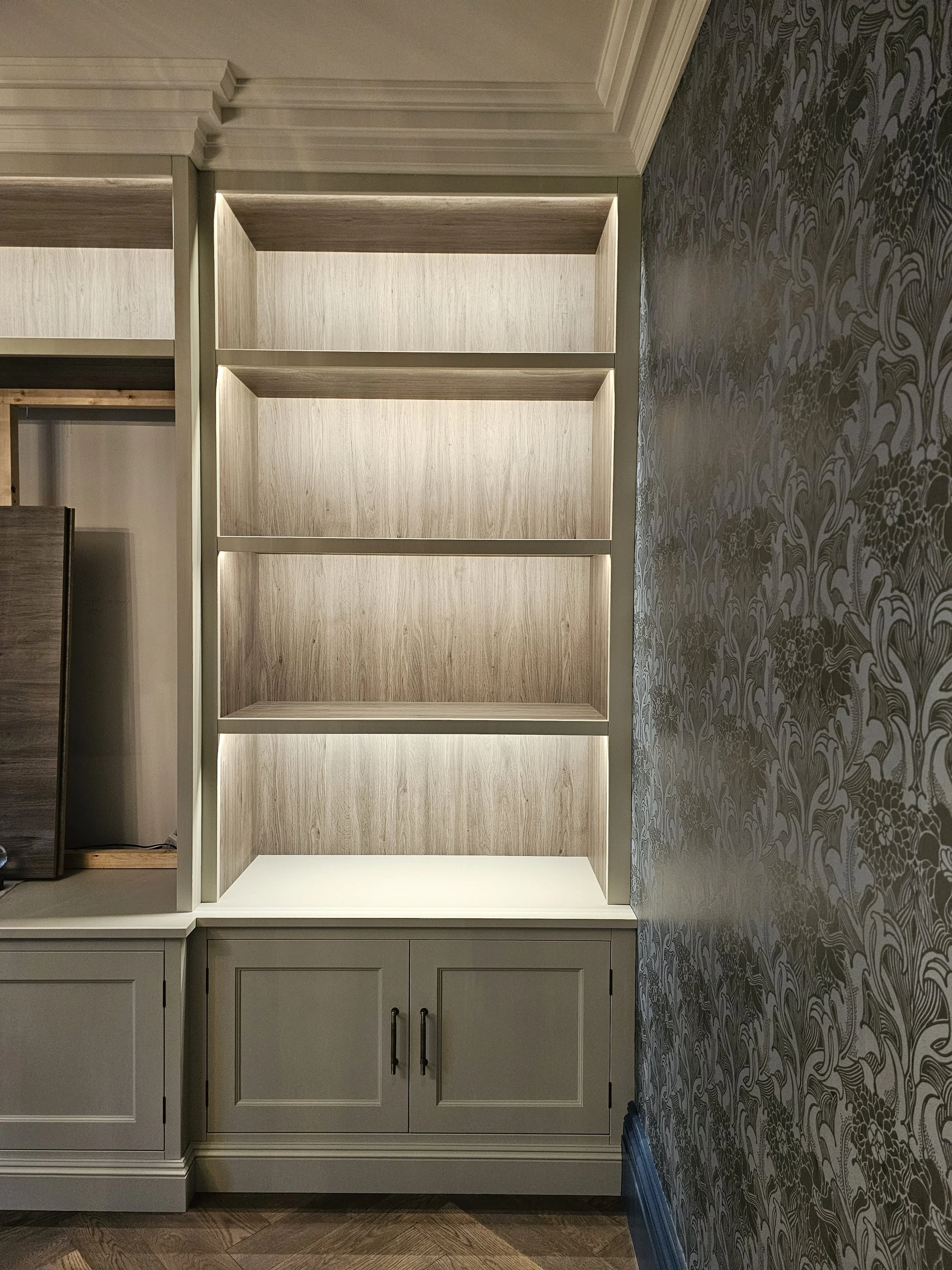 Built-in bookshelf with four empty shelves and lower cabinet, located against a wall with patterned wallpaper.