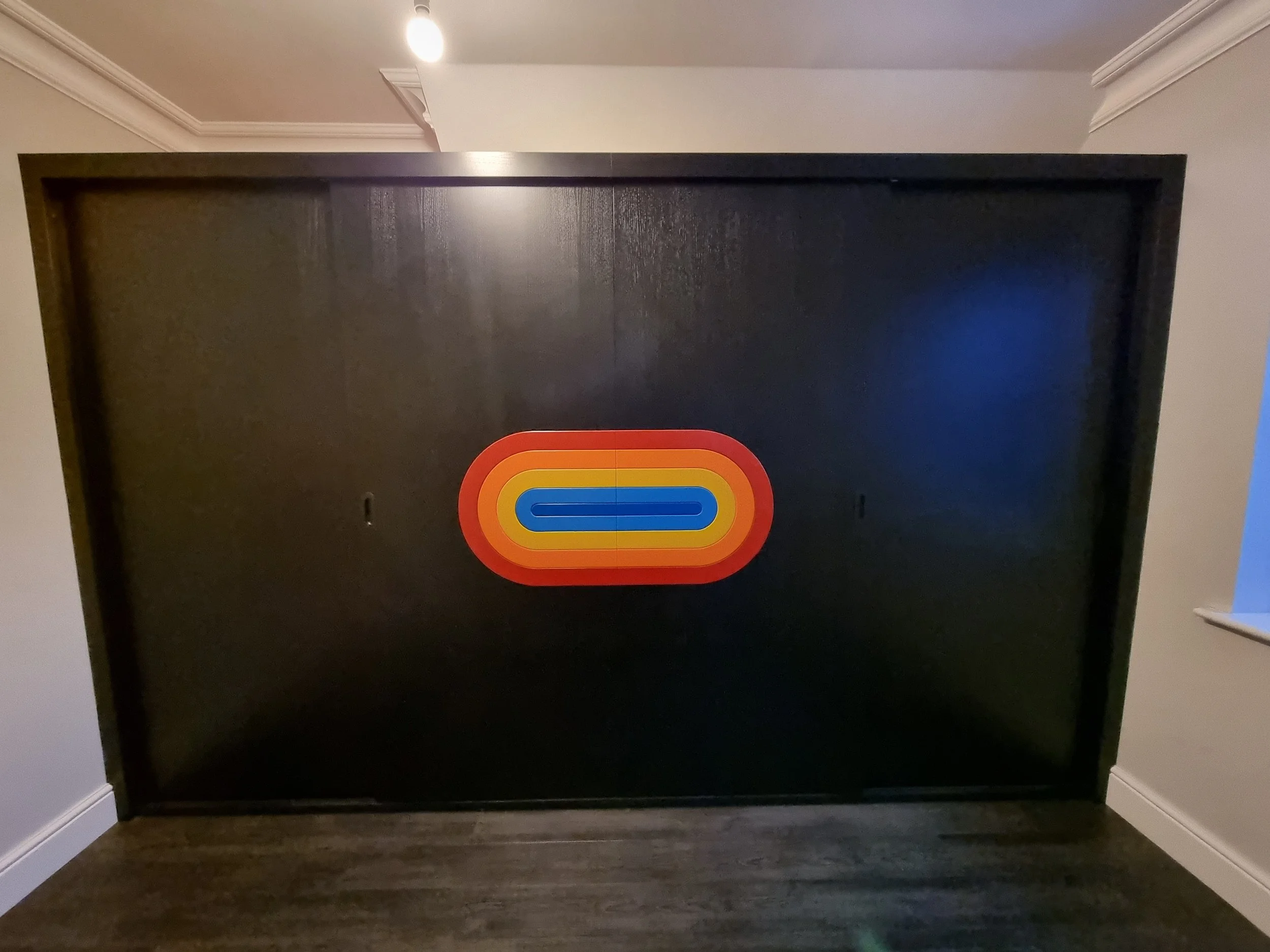 Back of a black television with a colorful retro logo, placed on a dark wood surface in a room with gray walls and white crown molding.