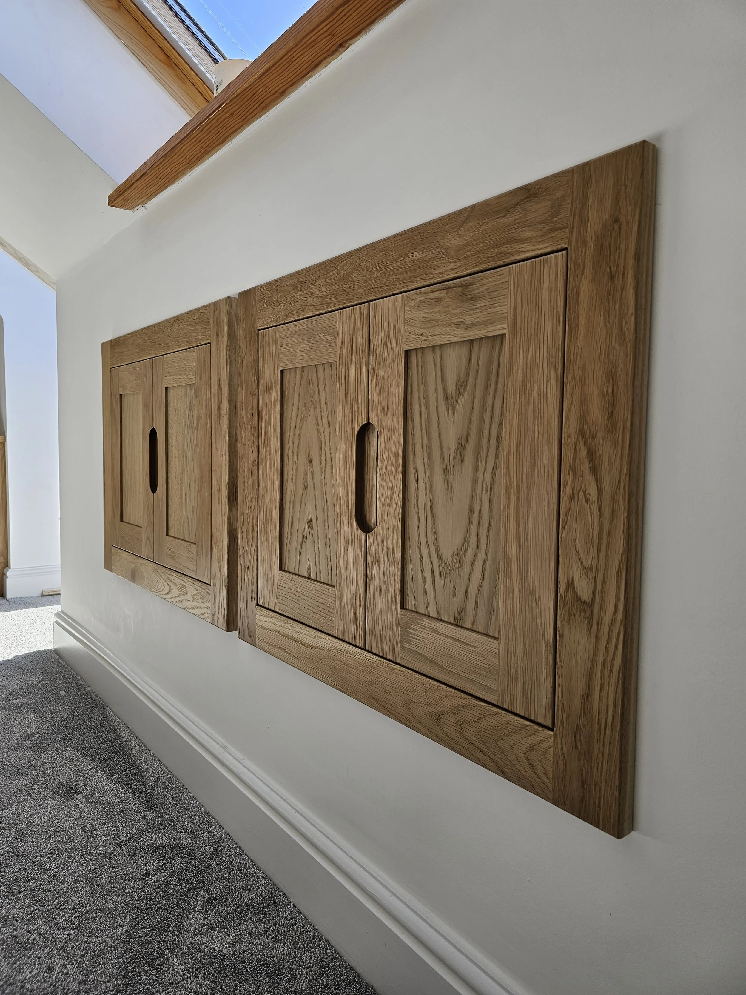 Wooden recessed cabinet with sliding doors built into a white wall.