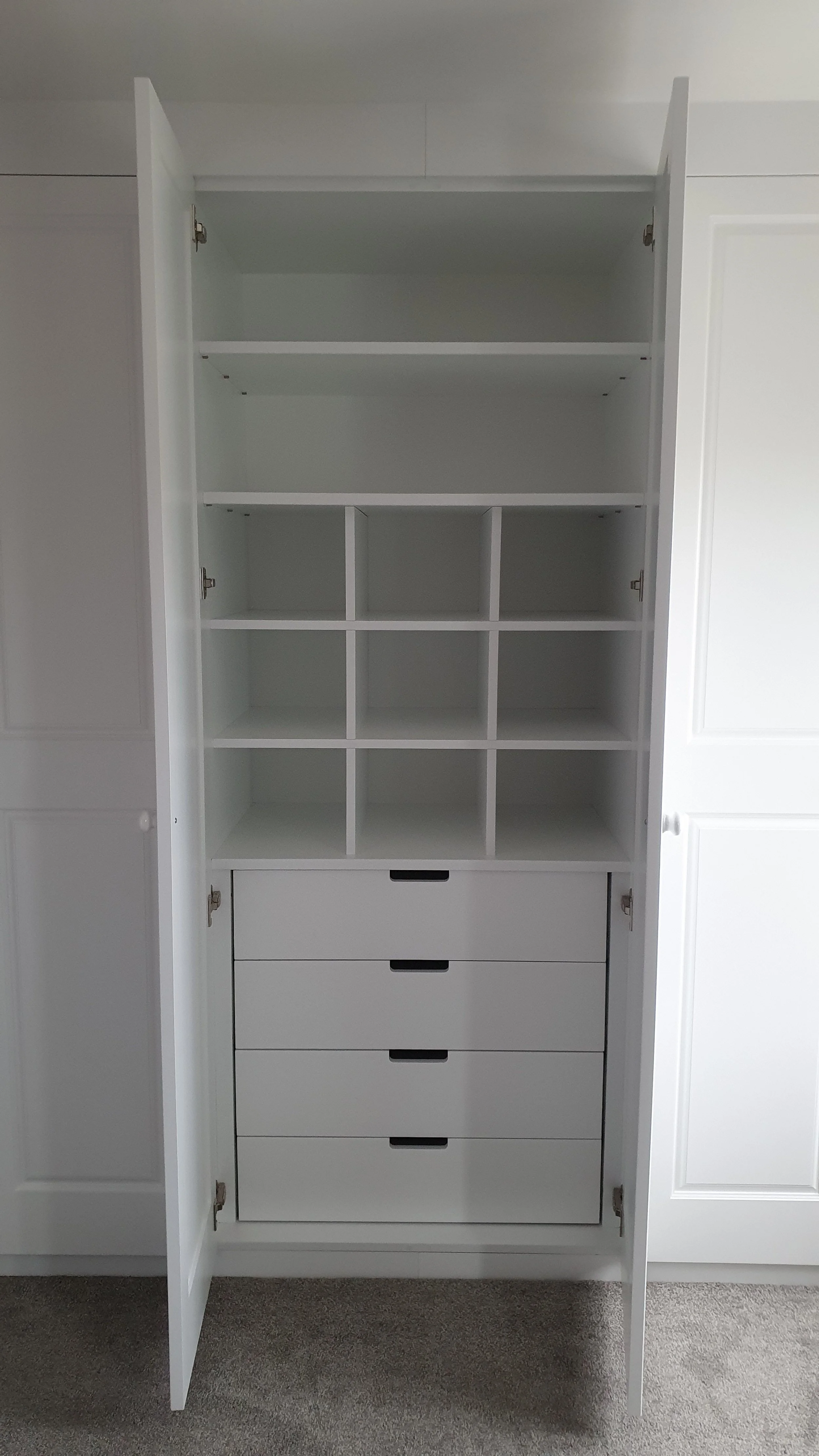 Open white cabinet with multiple shelves and drawers, situated against a wall.
