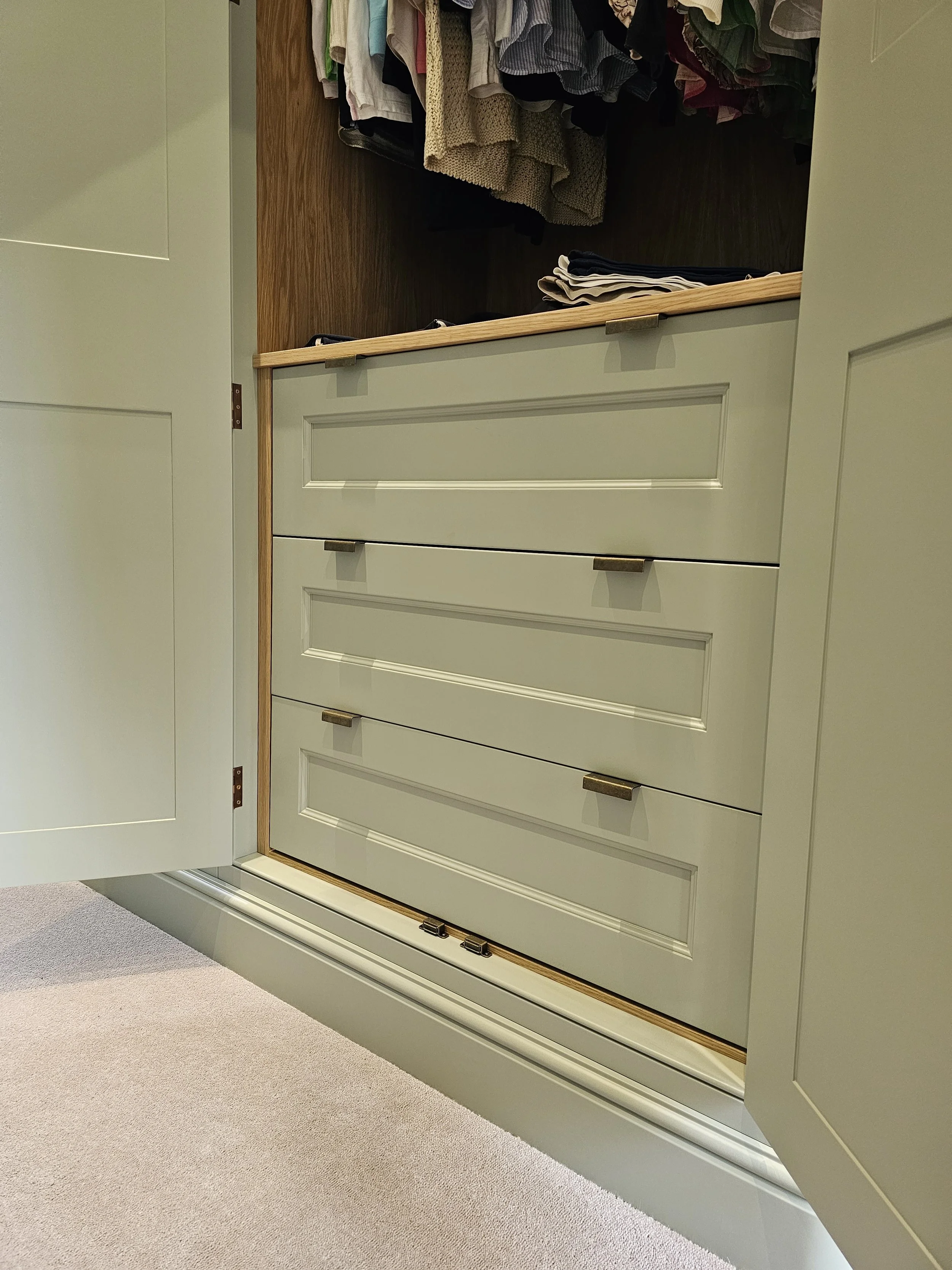 Open closet with light green cabinets and drawers, showing hanging clothes above and folded clothes on the shelf.