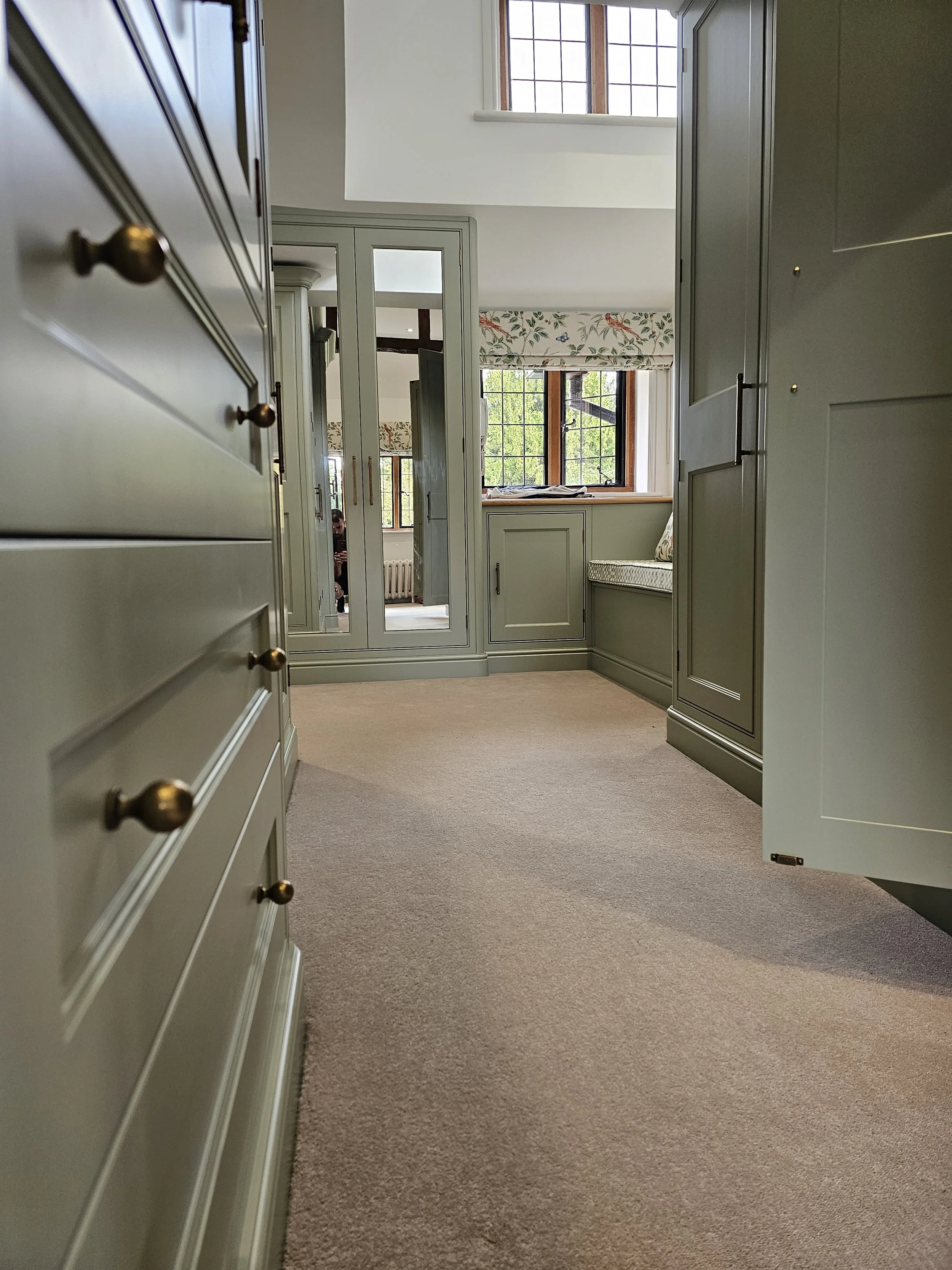 Interior view of a cozy room with built-in green cabinetry, large windows with floral valances, and a beige carpet.