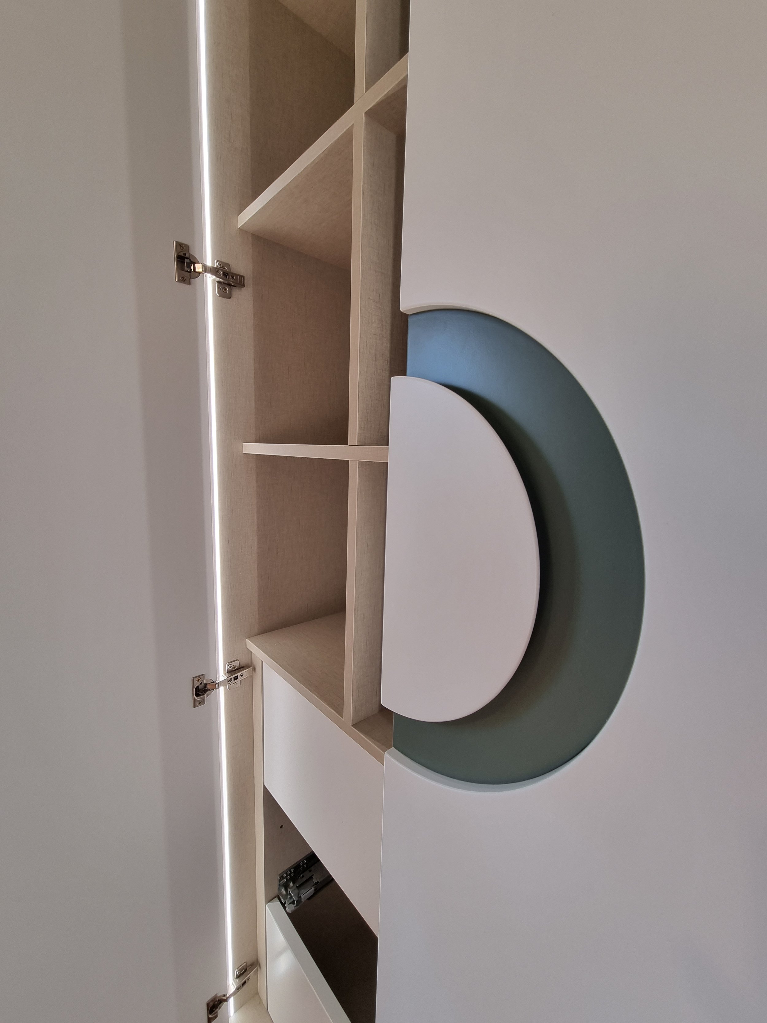 Open cabinet with multiple beige shelves and a decorative circular object with a semi-circular cutout in front, set against a white background.