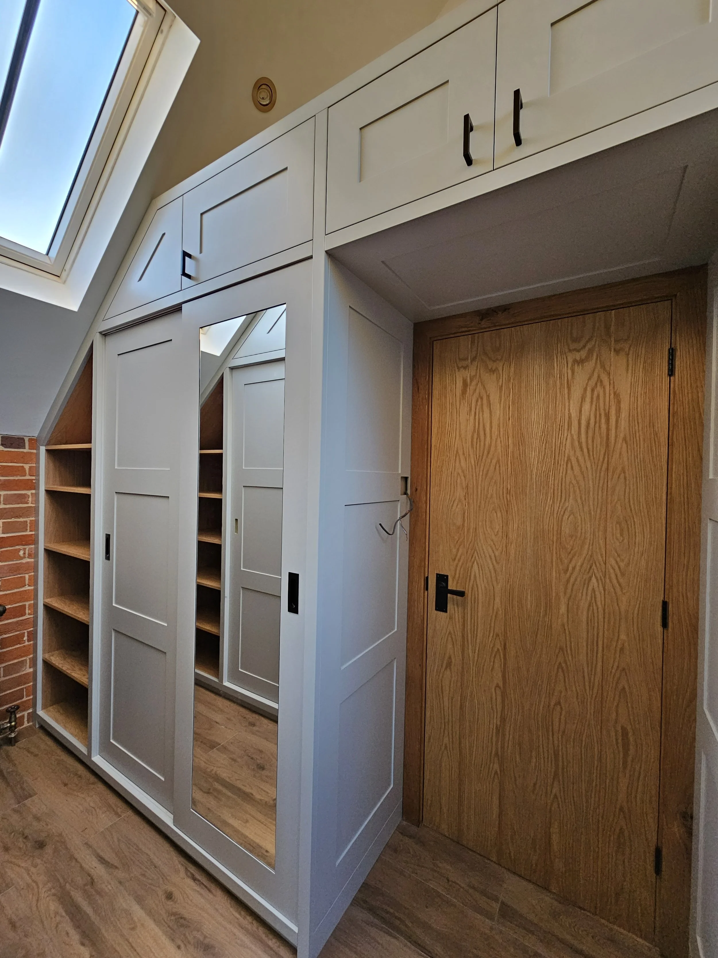Interior view of a room with white built-in cabinets, a wooden door, and a sloped ceiling with a skylight window.