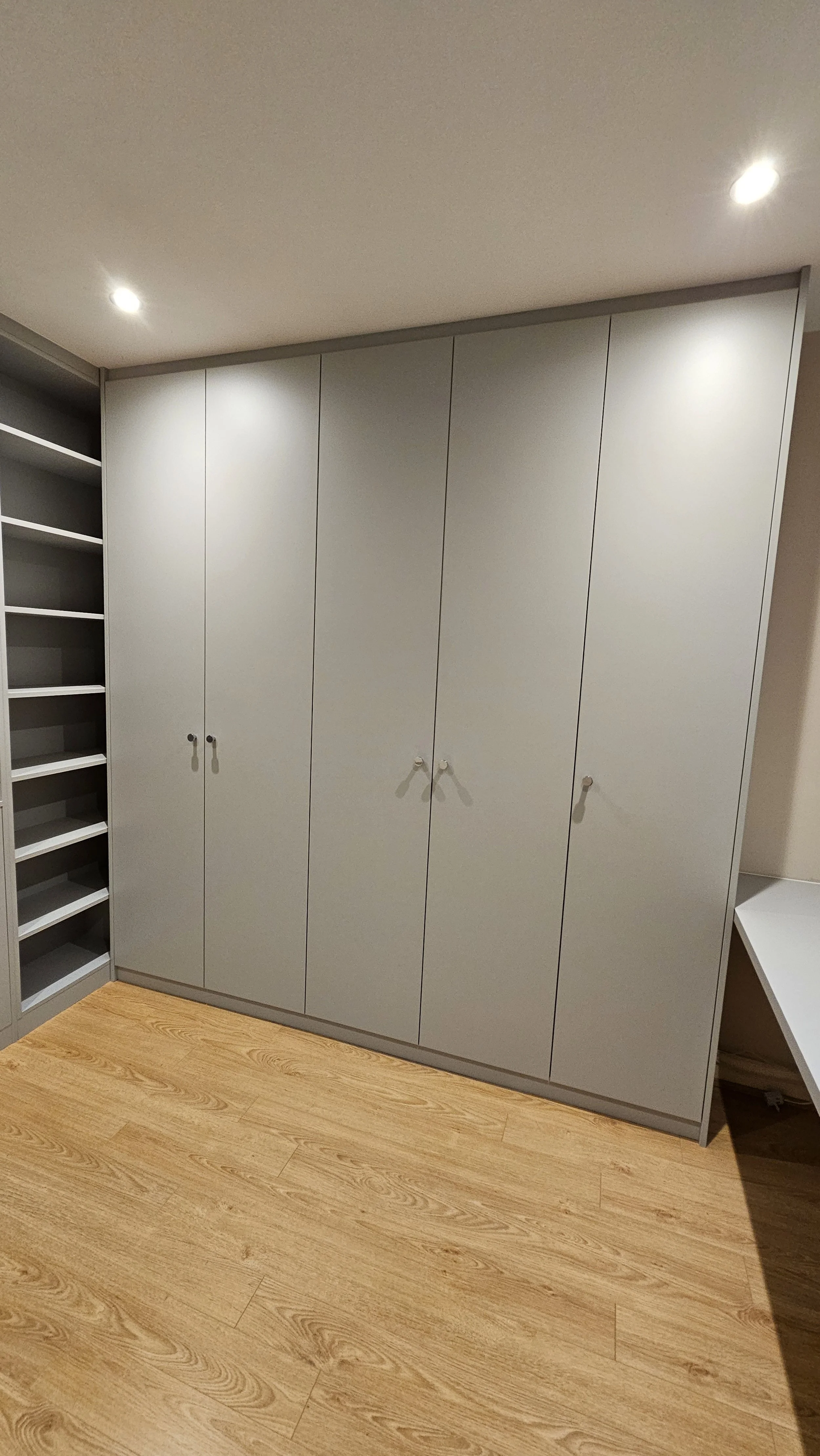 A gray wardrobe with four doors in a room with wooden flooring.