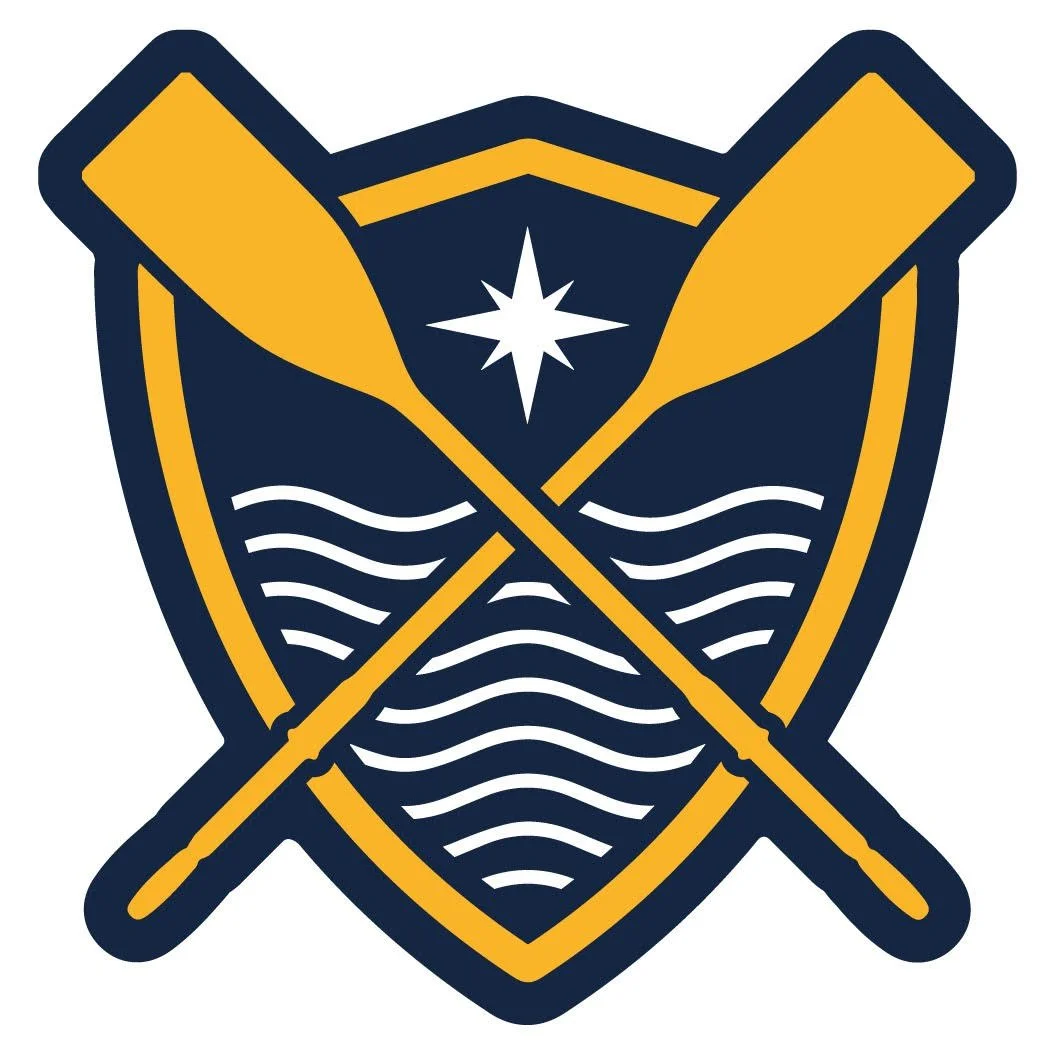 Seas The Day Logo- A shield emblem with two crossed paddles, a star, and wavy lines, featuring navy blue and gold colours