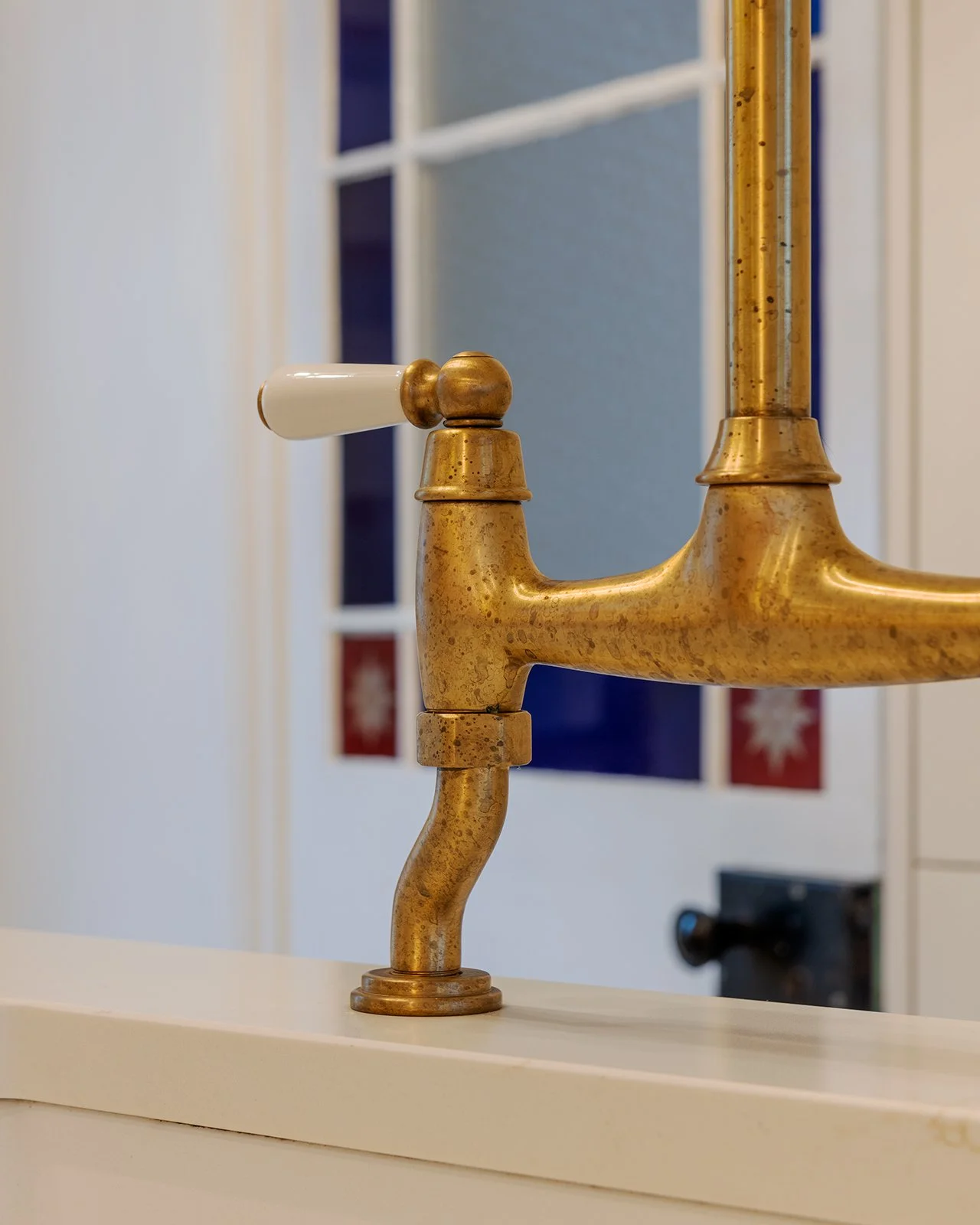 Close-up of a vintage brass faucet with a white ceramic handle, mounted on a white counter, with a tiled wall in the background.