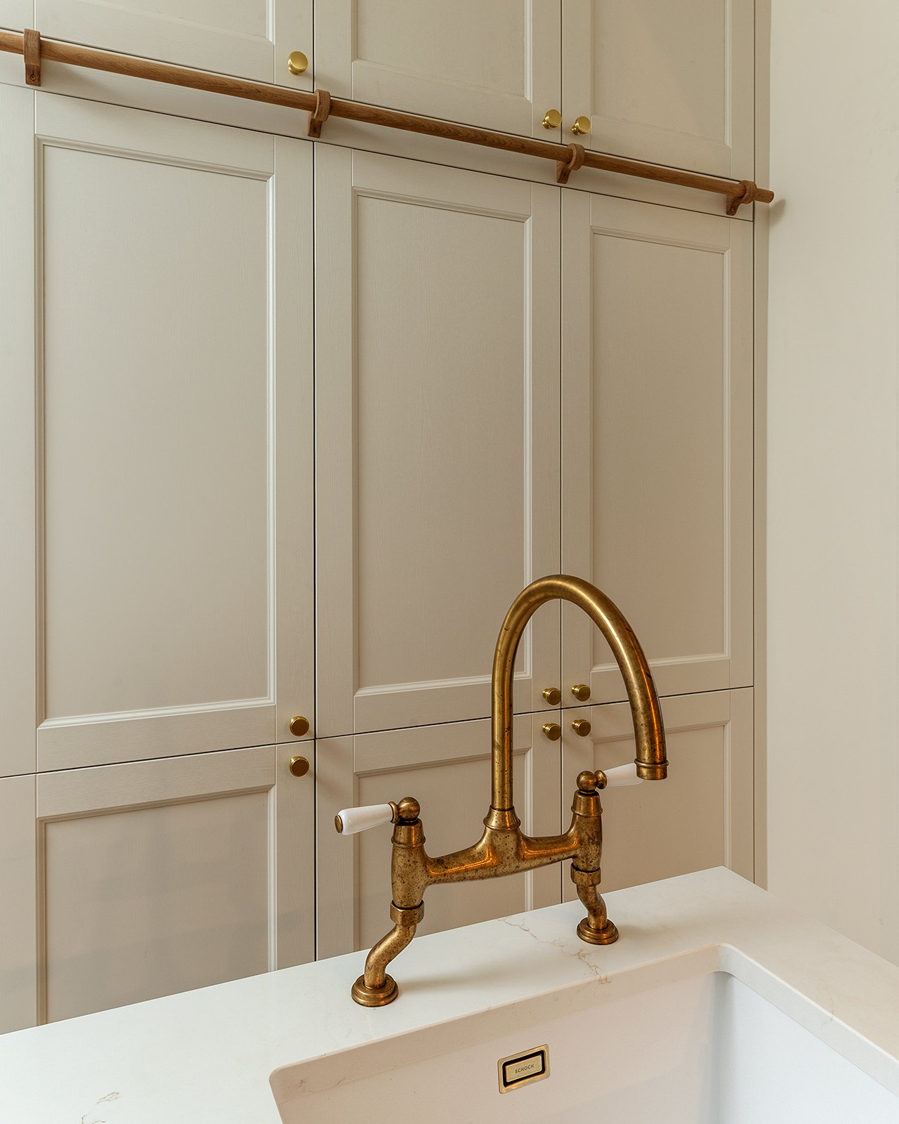 Kitchen with beige cabinets, a marble countertop, and a gold faucet above a white sink.
