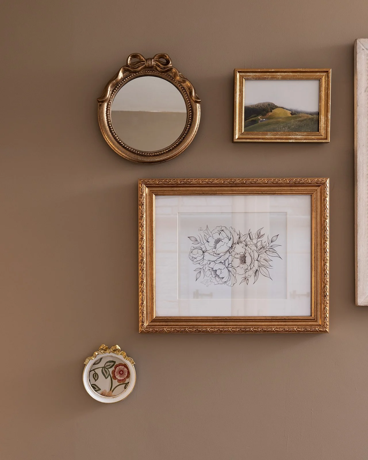 Wall with five decorative picture frames, including a round mirror, a landscape photograph, a line drawing of flowers, a small floral artwork, and part of a large canvas