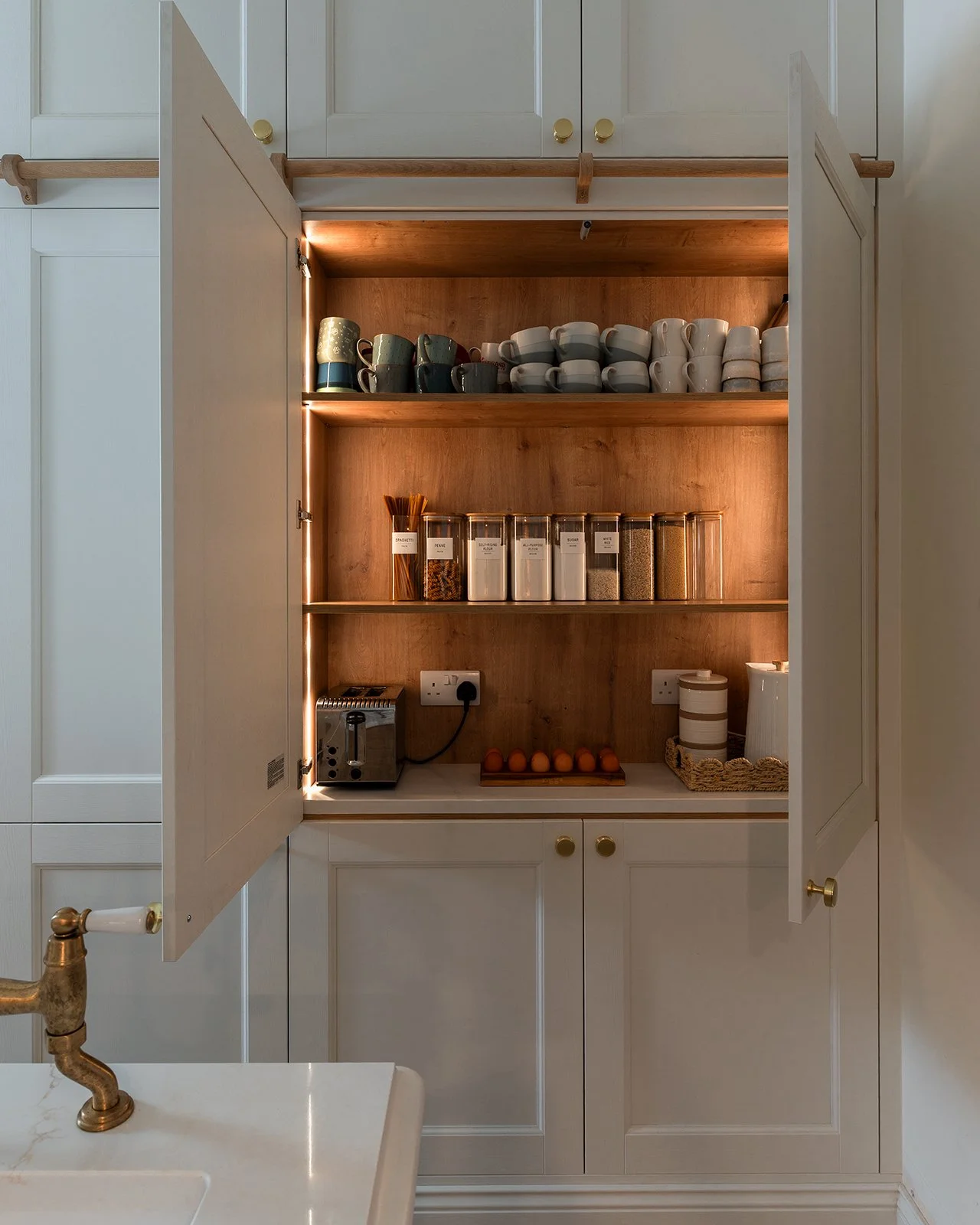 Open kitchen cabinet with cups, jars of spices, eggs, and a toaster inside.
