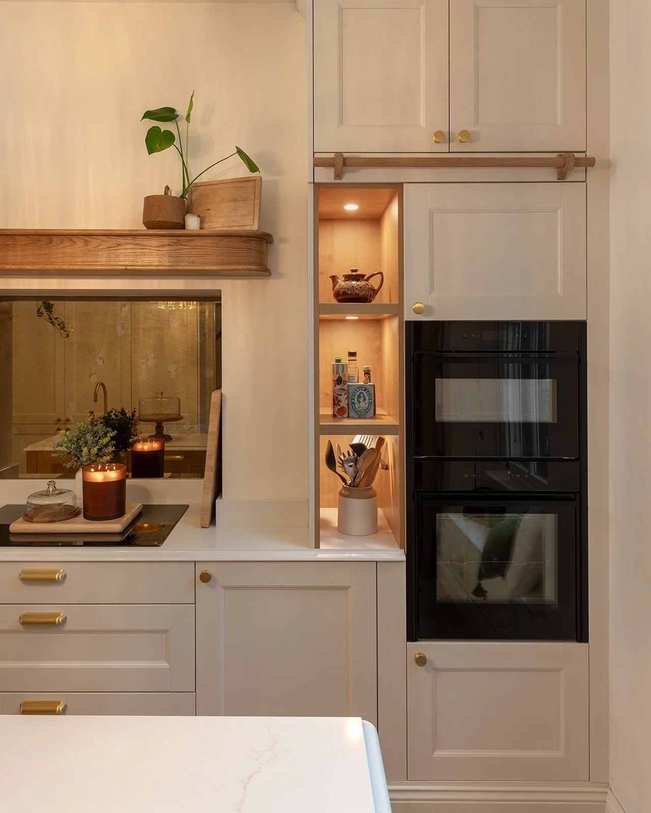 Kitchen with cream cabinets, black oven, open wooden shelves with teapot and spices, marble countertop, candles, and decorative items.