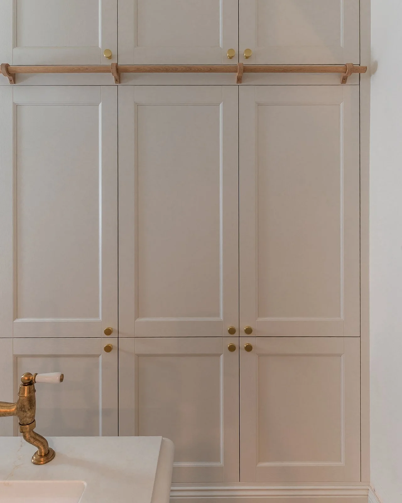 A kitchen cabinet with multiple doors, gold knobs, and a wooden towel rack above it. Part of a white sink with a gold faucet is visible in the foreground.