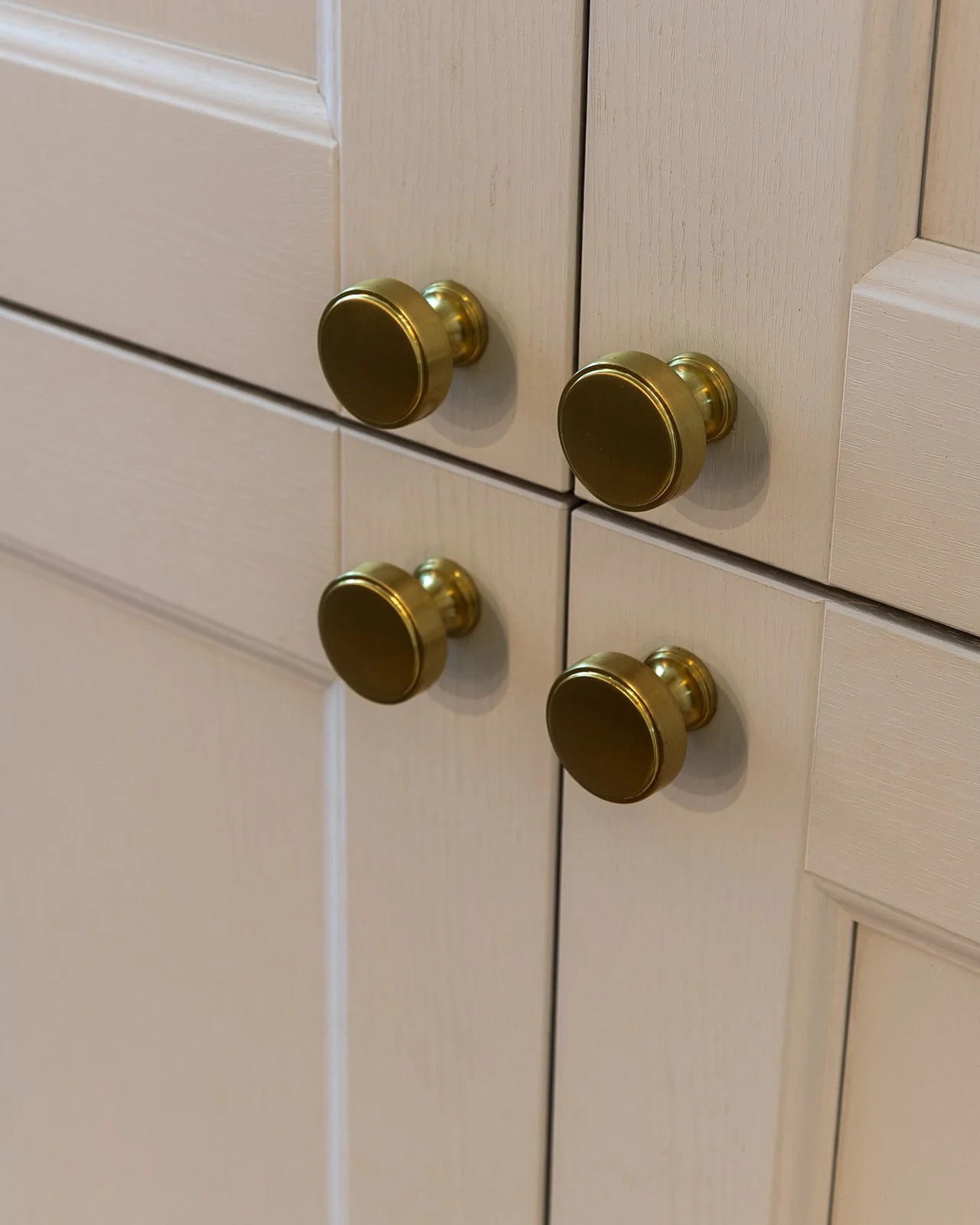 A close-up of beige kitchen cabinets with brass knobs.