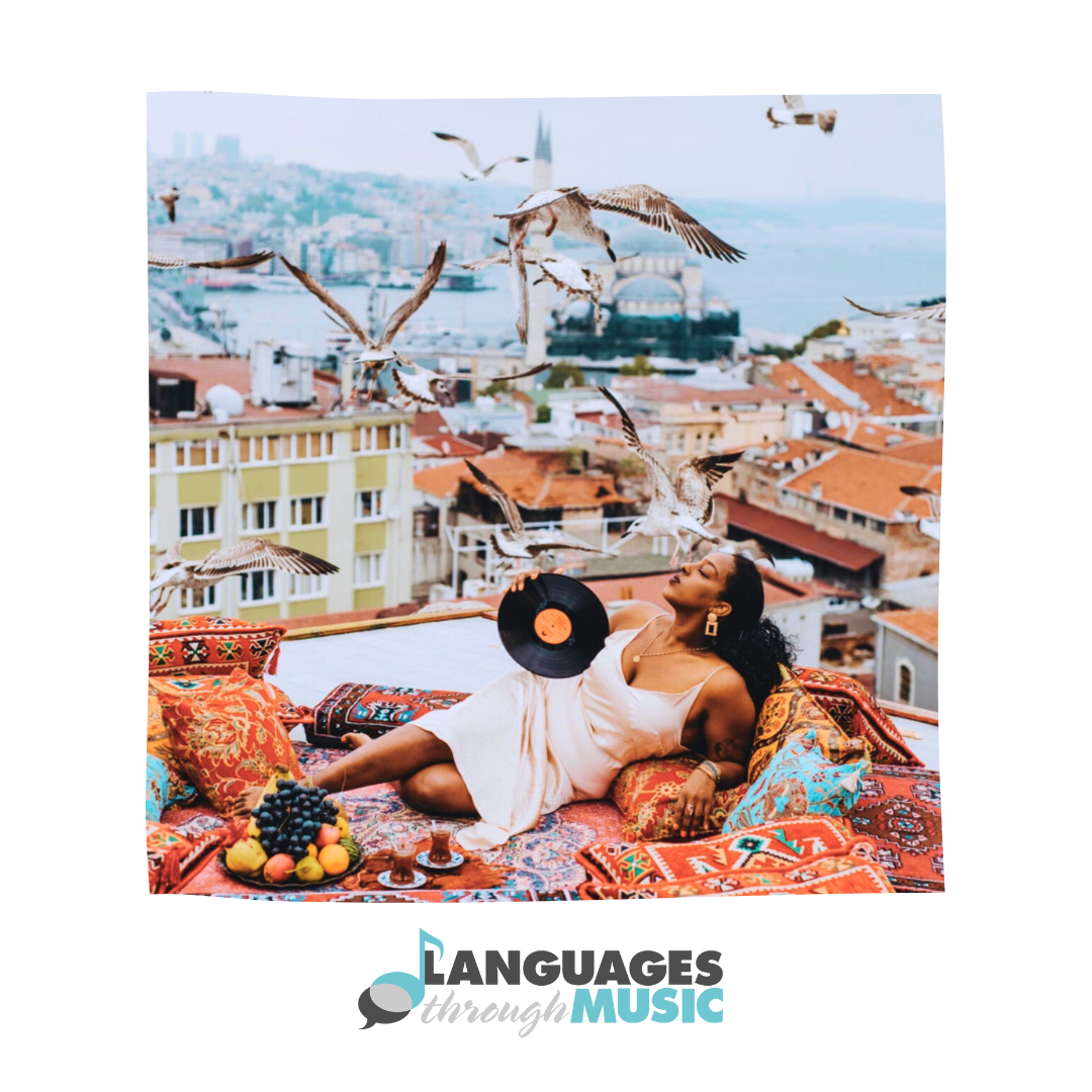 A woman relaxing on a rooftop surrounded by colorful cushions and a fruit platter, while holding a vinyl record. Birds are flying overhead against a cityscape background with a river and buildings.