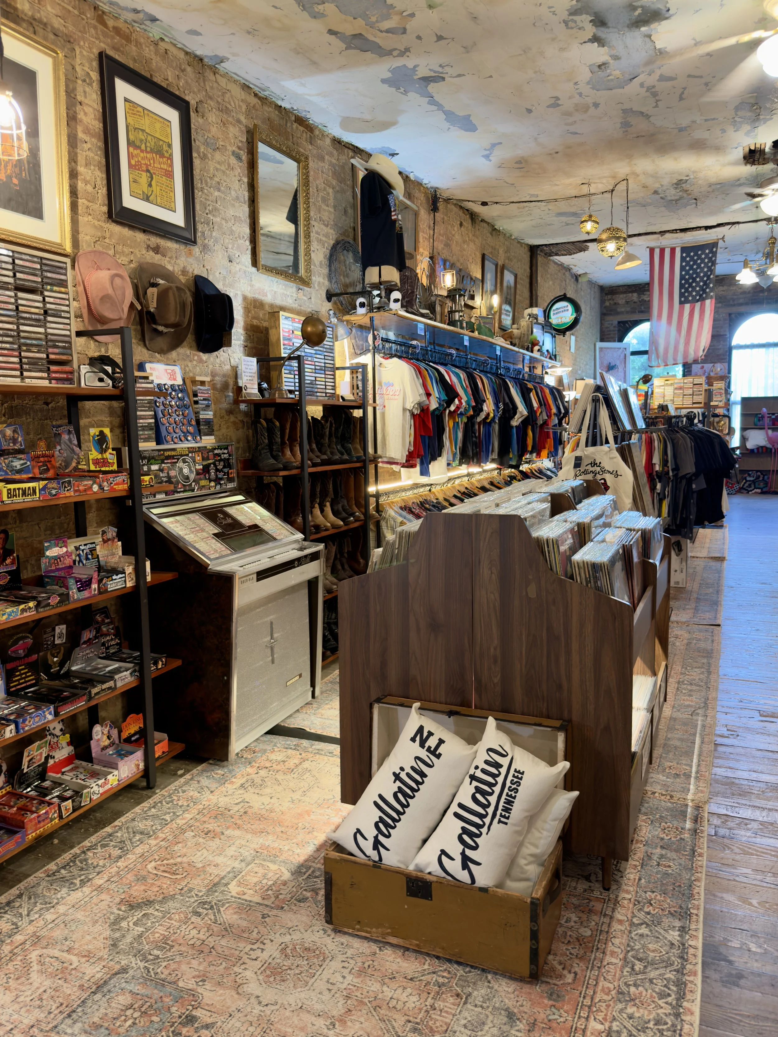 Inside a vintage store, Vintage 5, with exposed brick walls, displaying clothes, vinyl records, cassette tapes, hats, band shirts, clothes, wall art, and souvenirs in Gallatin, Tennessee just north of Nashville, TN and near Hendersonville, TN.