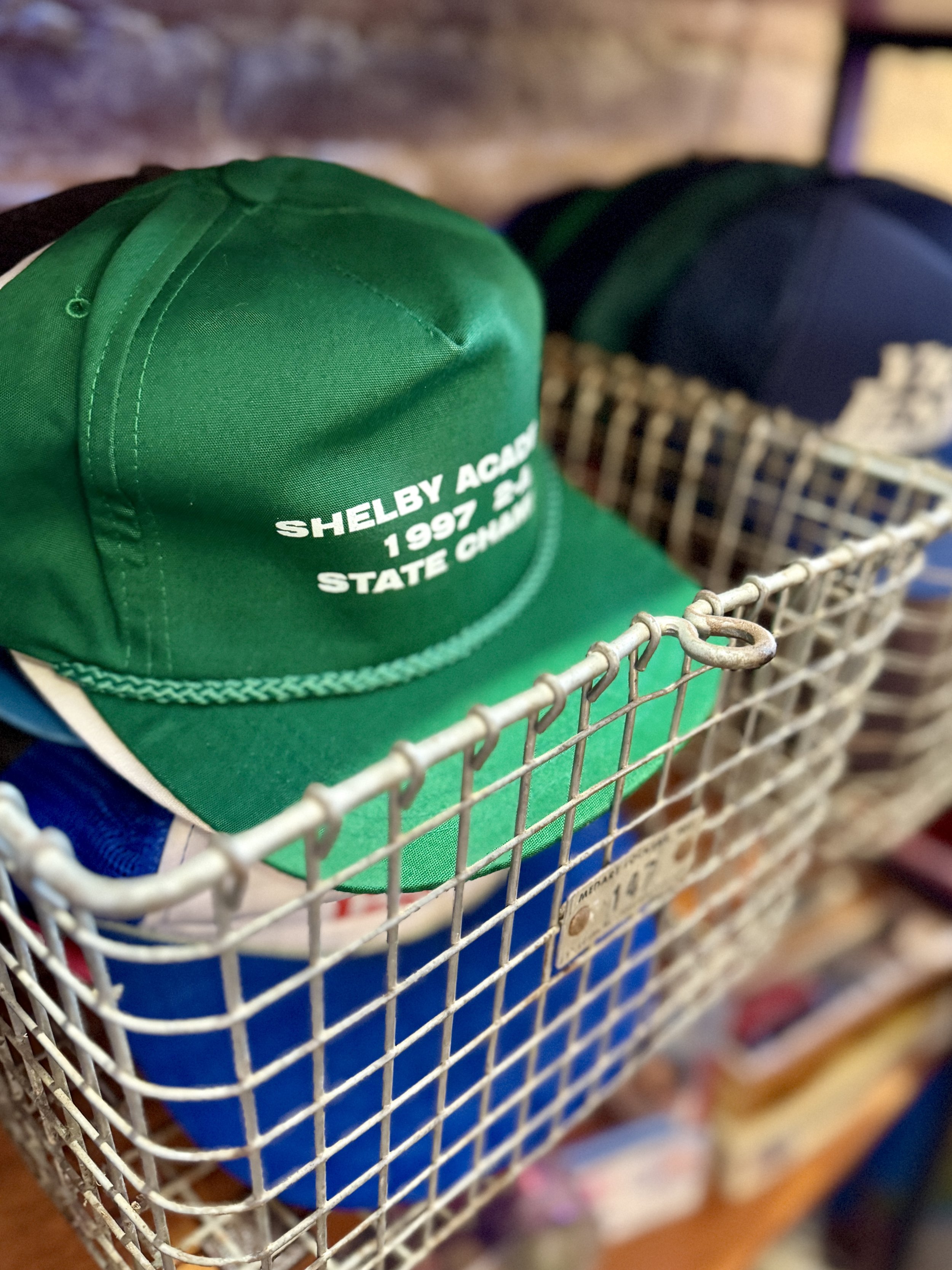 Wire basket of vintage baseball caps on a store shelf.