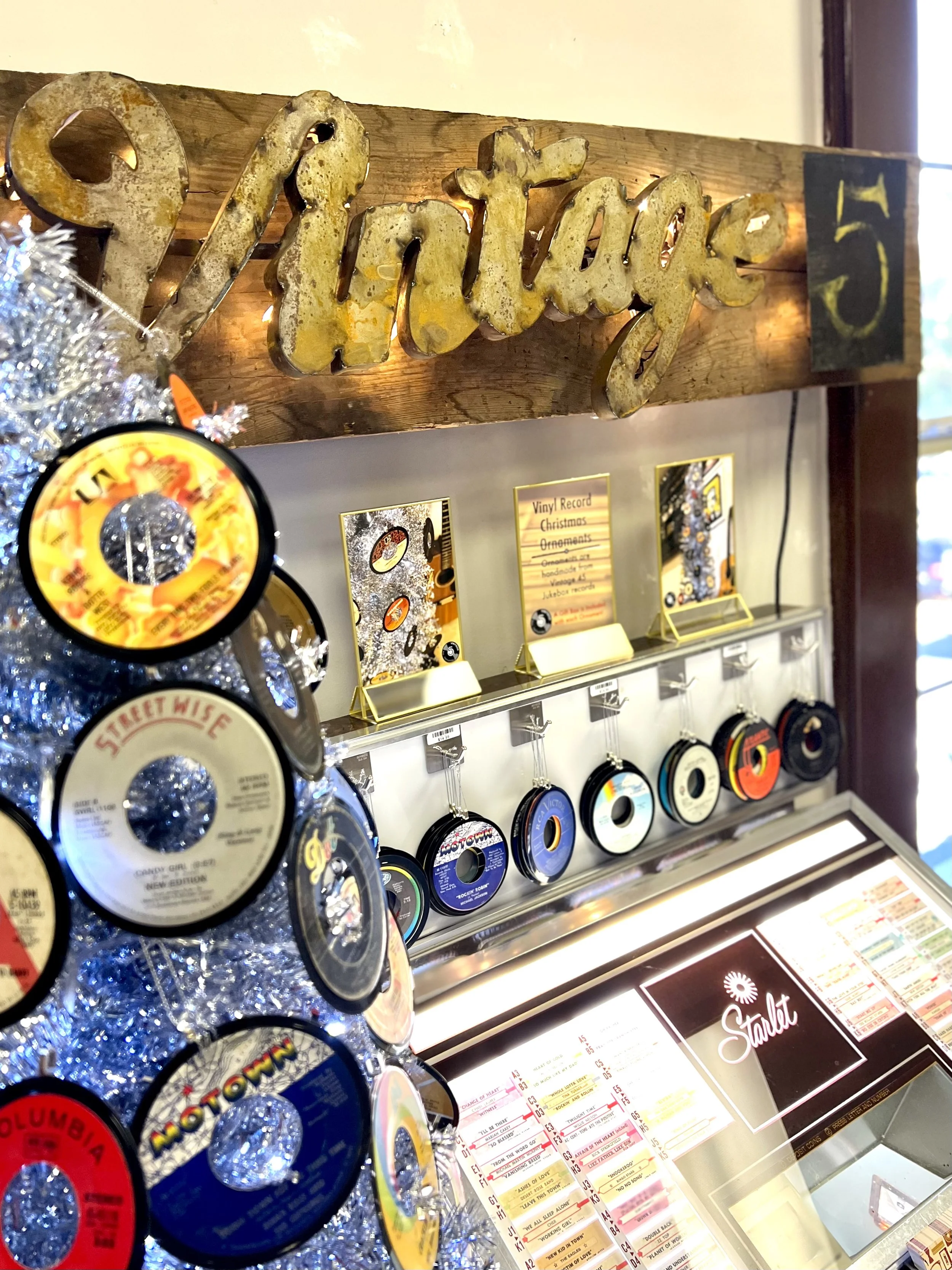 Vintage-themed display with a wooden 'Vintage' sign, hanging vinyl records, and a retro jukebox. Records serve as ornaments on a silver tree. Labels include 'Streetwise,' 'Motown,' and 'Columbia.'
