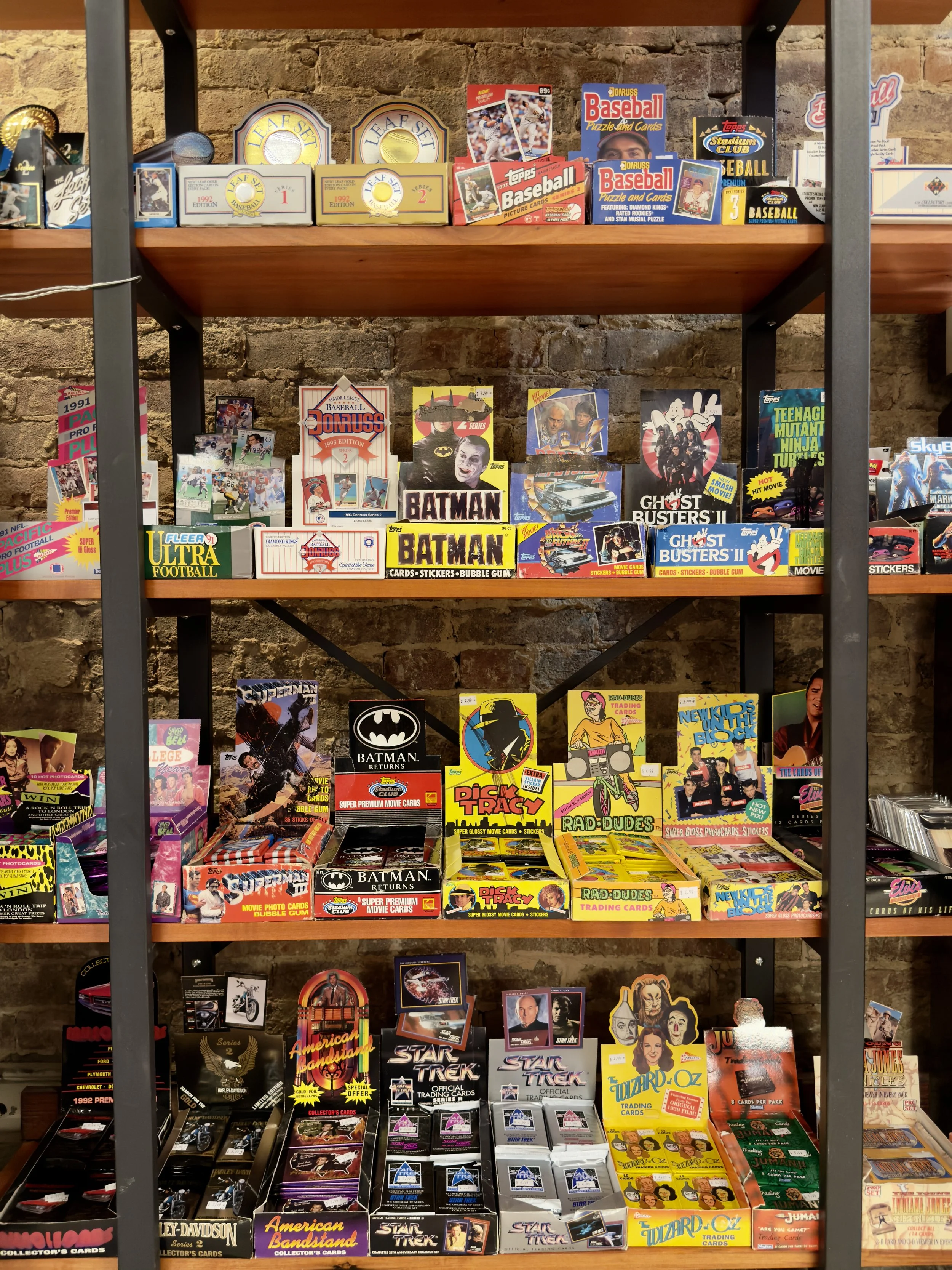 Shelf displaying vintage trading cards, including baseball, basketball, football, soccer, Star Trek, Batman, Ghostbusters, Teenage Mutant Ninja Turtles, Back to the Future, and other pop culture themes in colorful packaging.