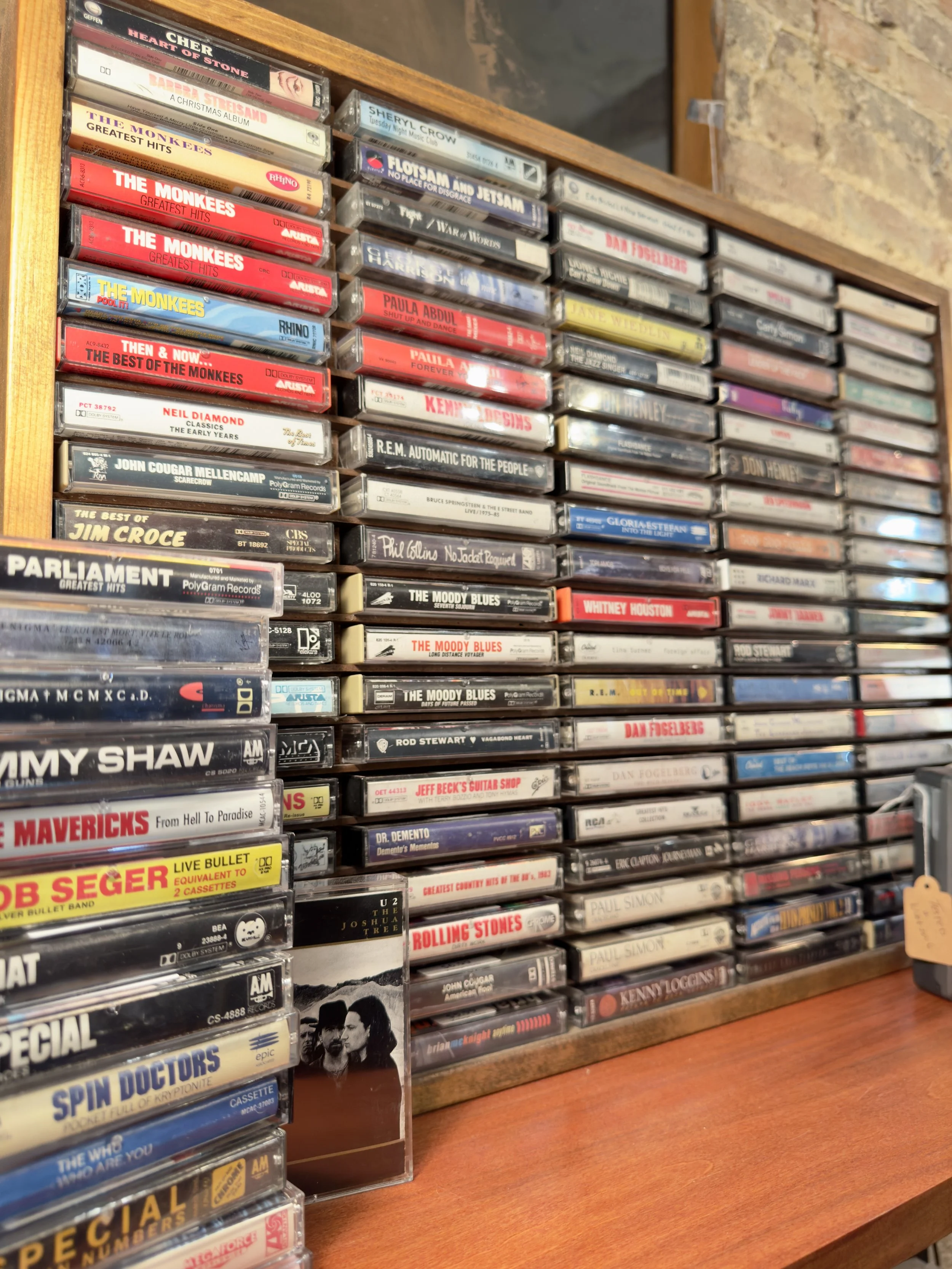 A wooden shelf filled with stacks of cassette tapes of various music artists and albums.