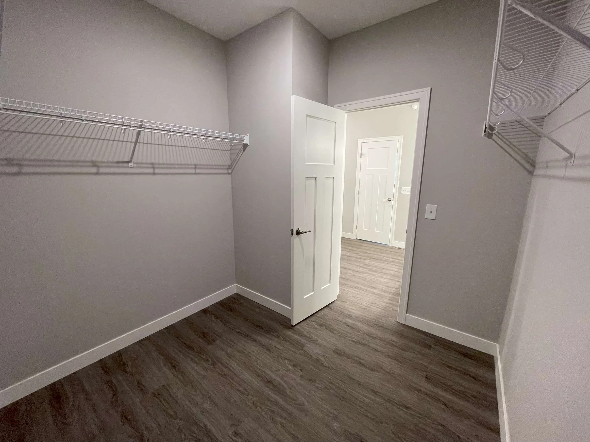 Empty walk-in closet with gray walls, wood flooring, and wire shelves—perfect storage in apartments in Rochester.