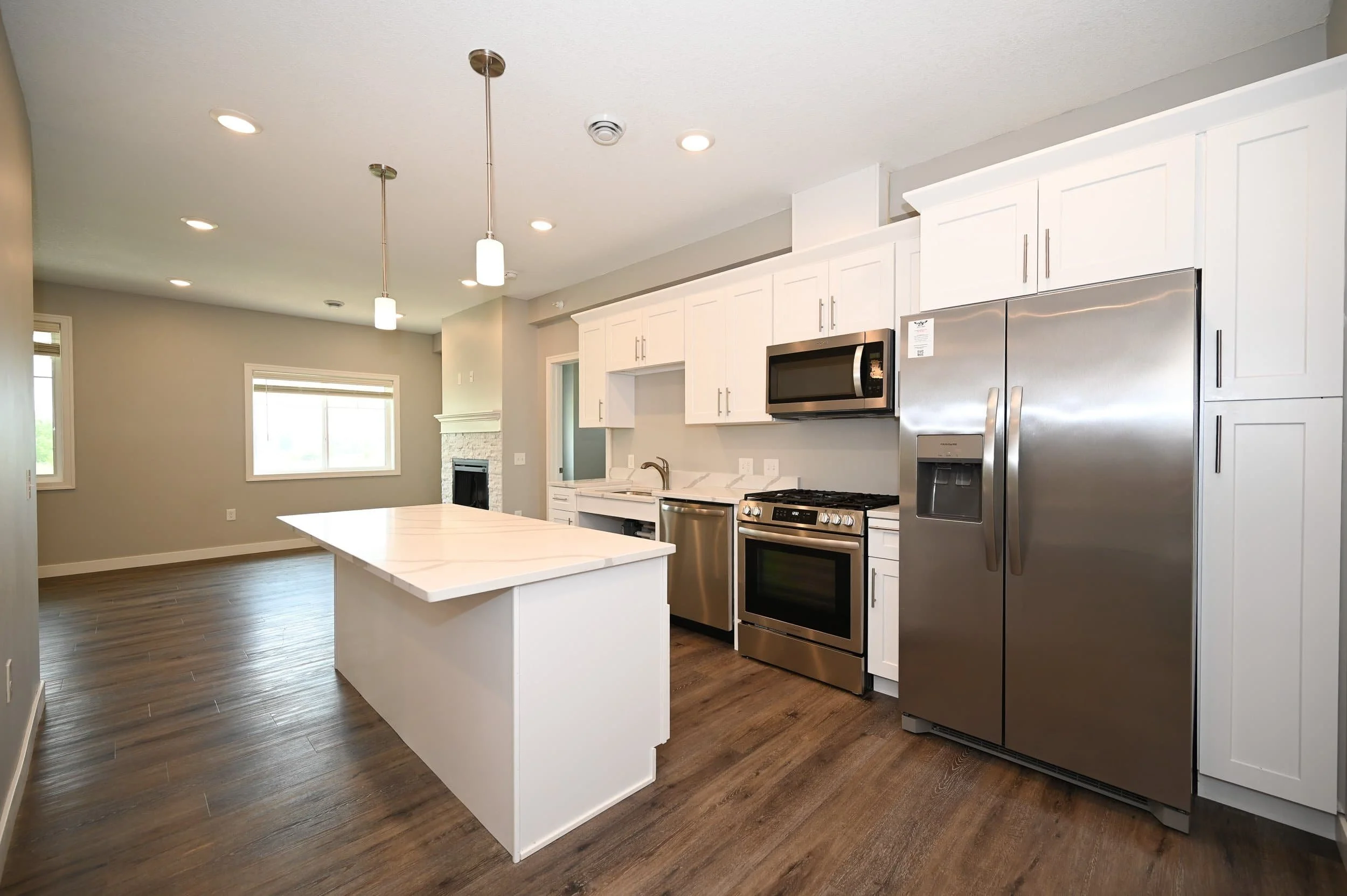 Modern kitchen in apartments in Rochester with white cabinets, stainless steel appliances, island, pendant lights, and wood flooring.