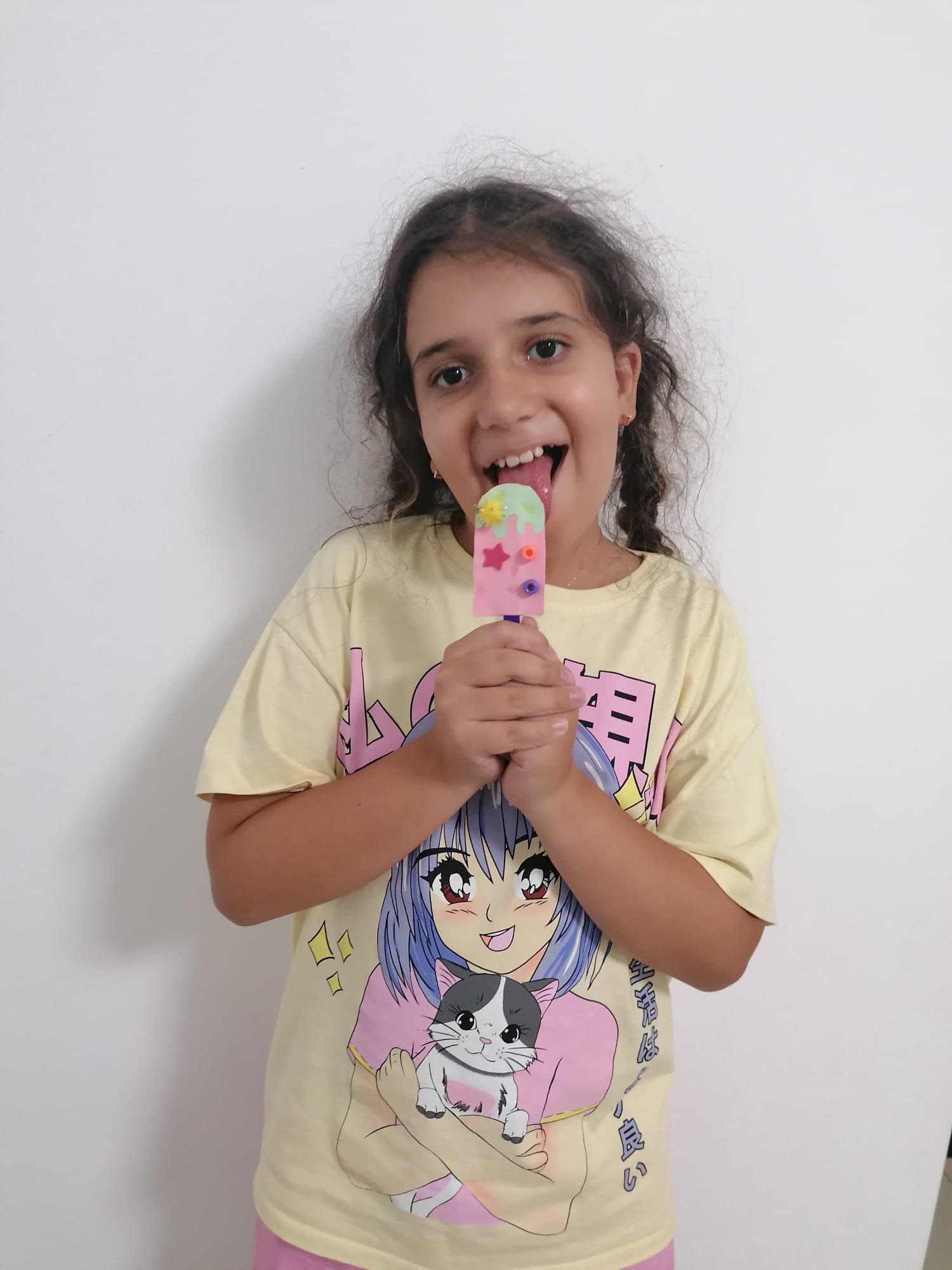 Child licking a colorful ice cream while wearing a T-shirt with an anime character on it.