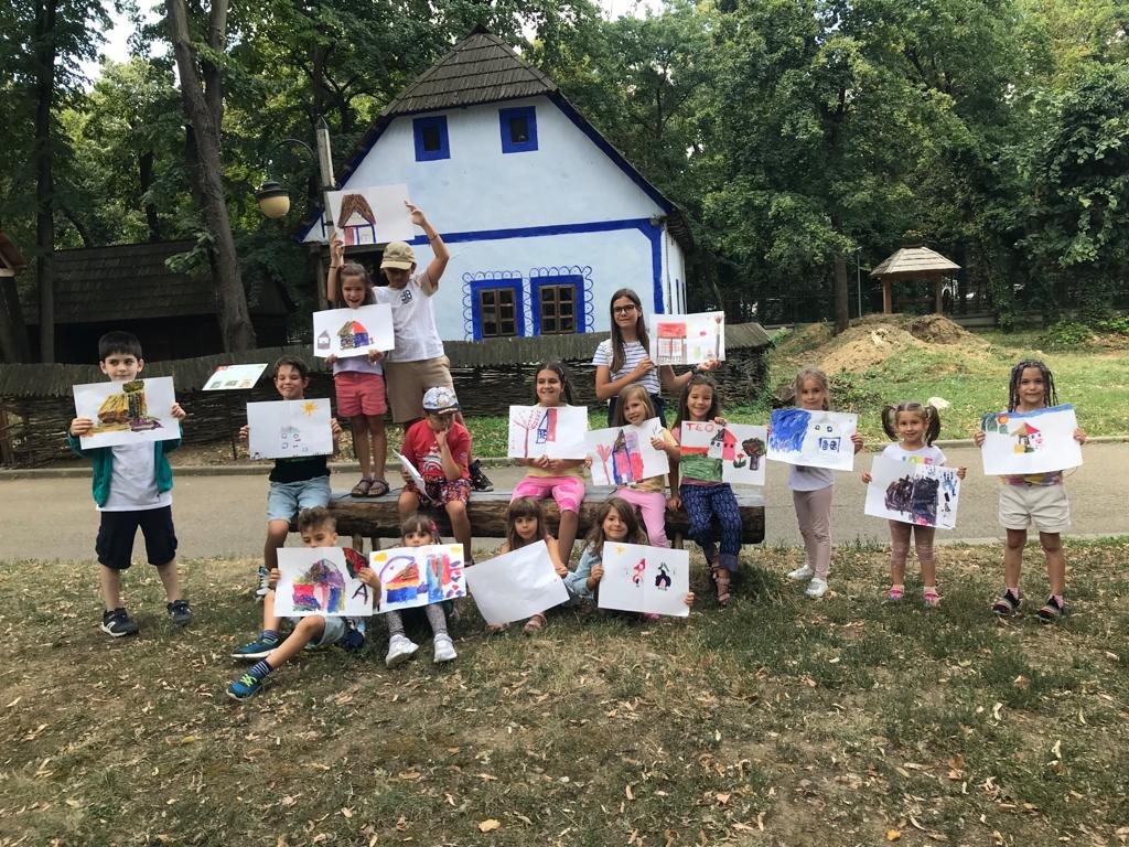 Group of children holding drawings in front of a blue and white house. Forest background.