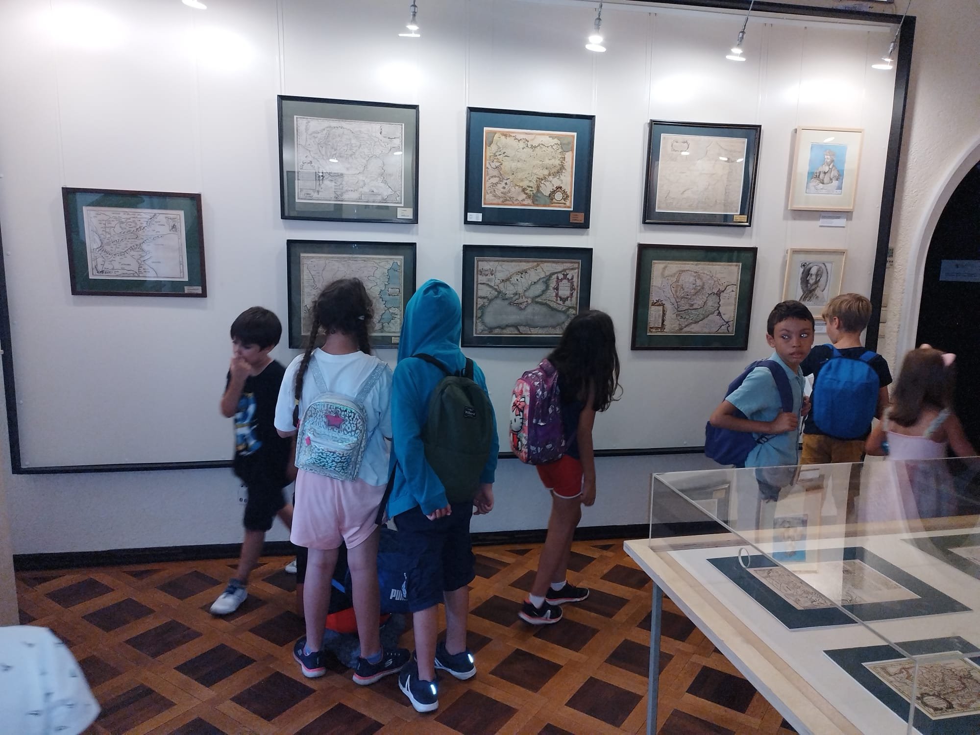 Children viewing framed historical maps on display in a museum room.