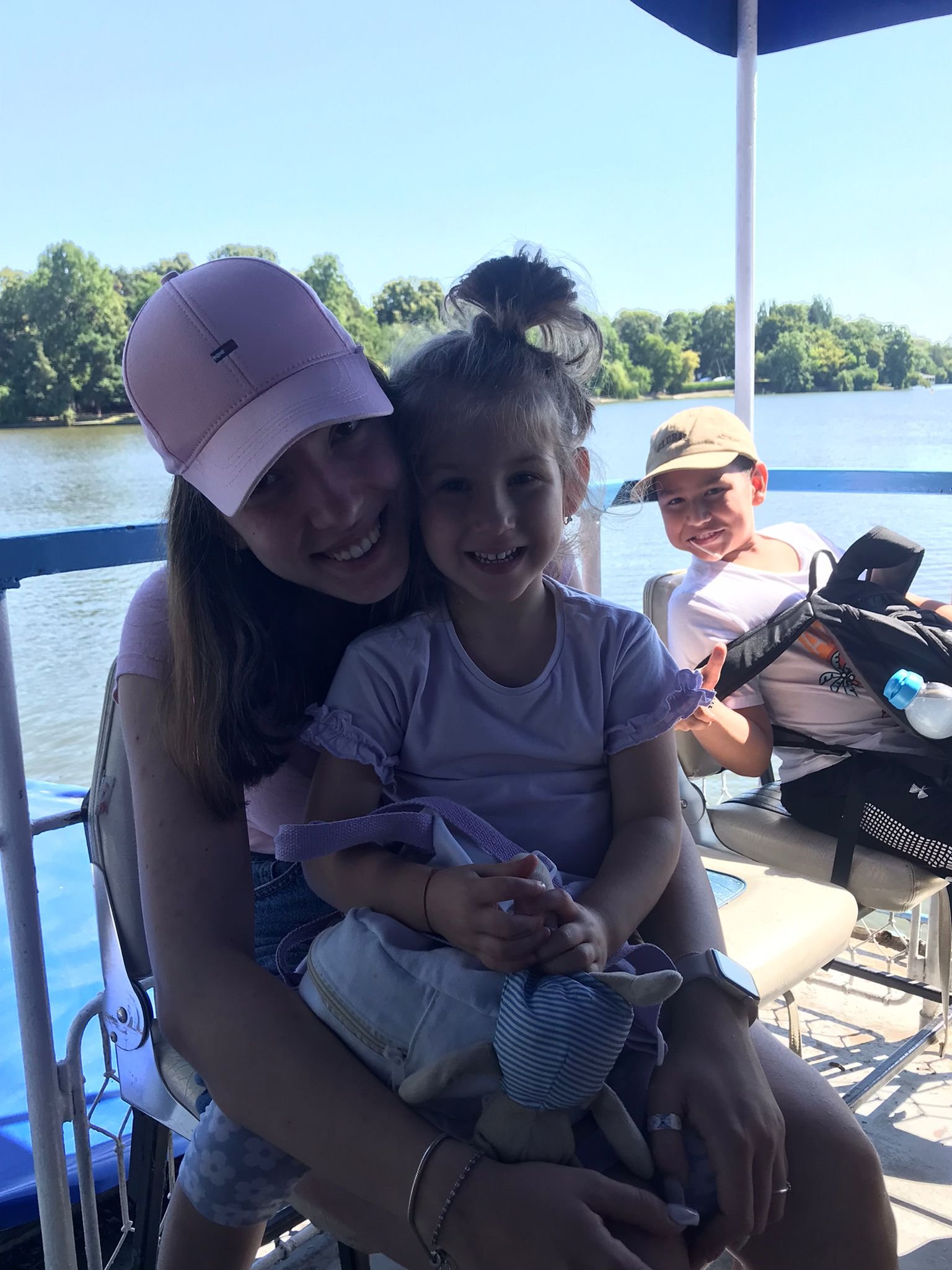 Two children and an adult on a boat, with water and trees in the background.