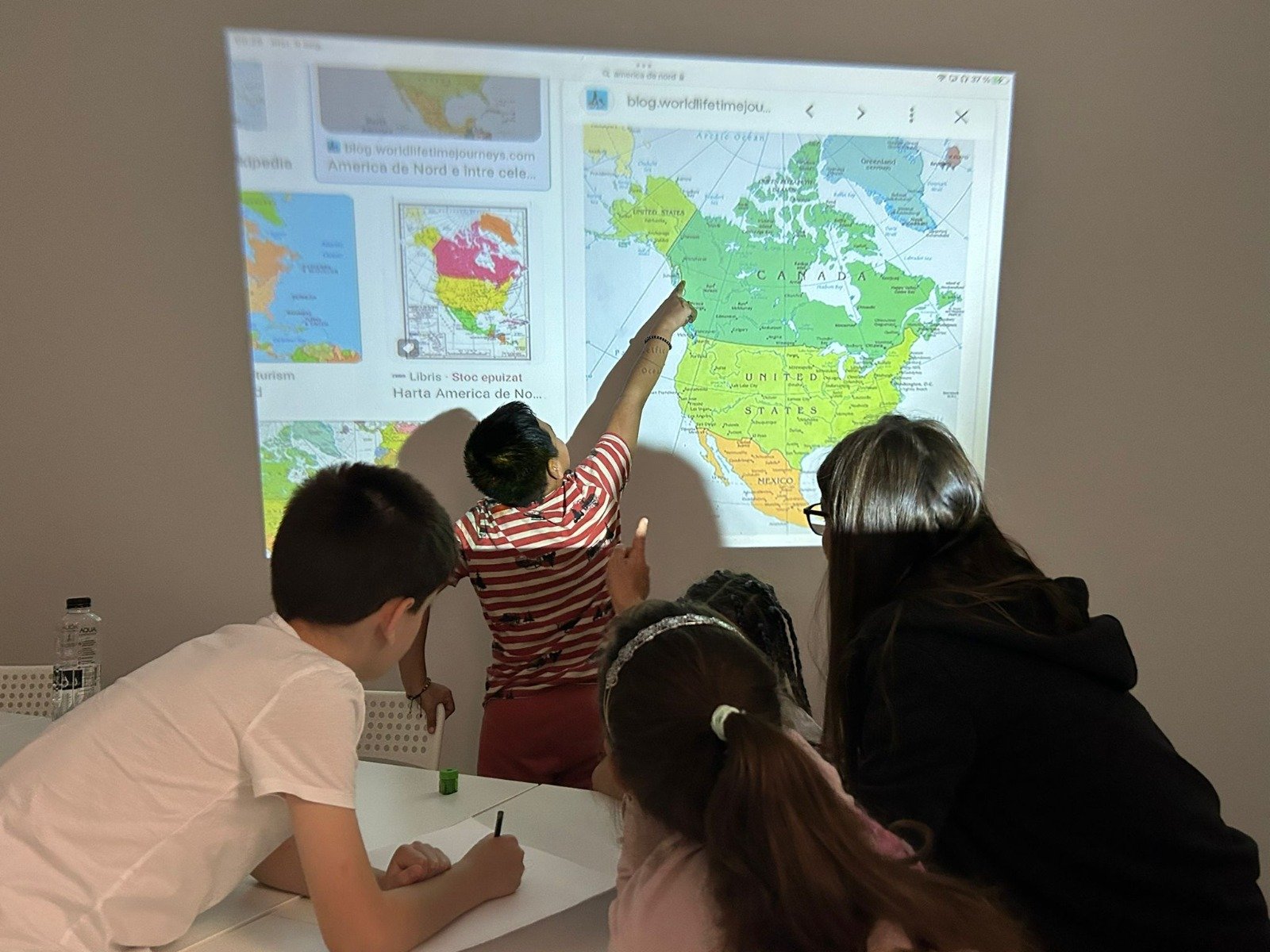 Children learning geography with a projected map of North America on the wall.