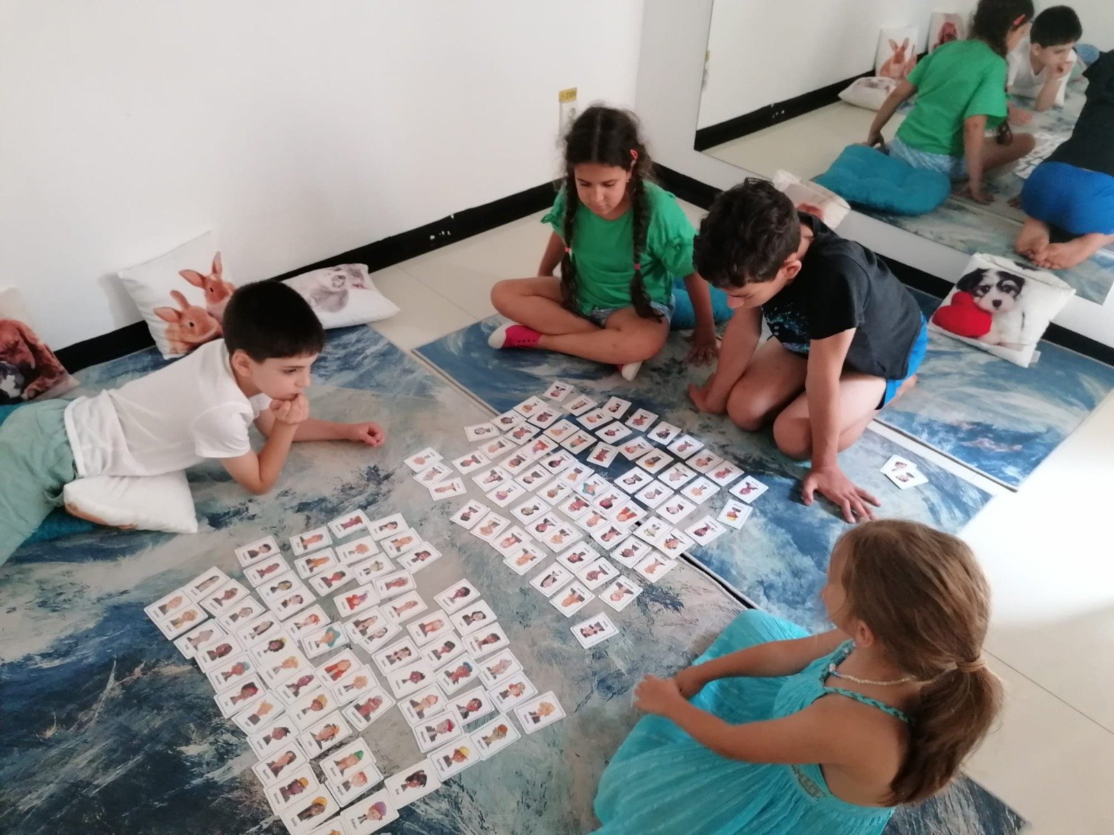 Children playing a card-matching game on the floor with animal pillows nearby.