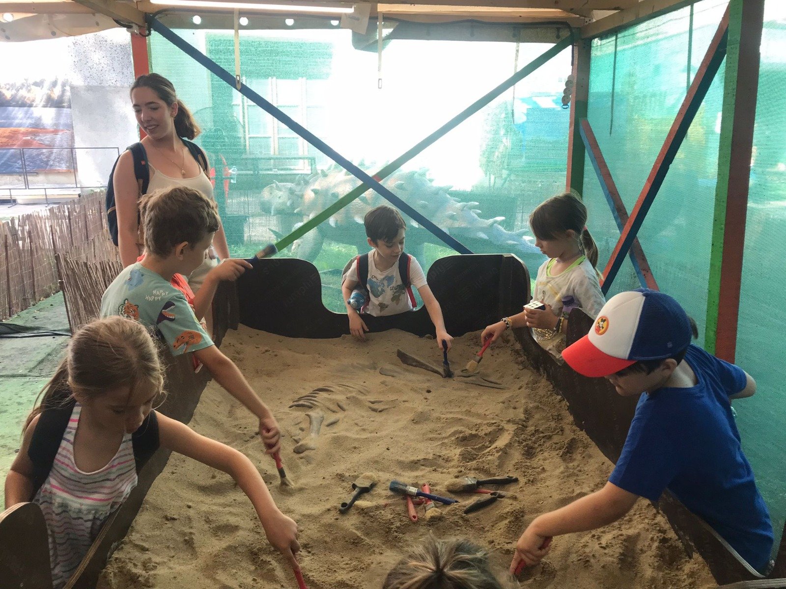 Children playing in a sandpit, using small tools to dig and explore. An adult is supervising the activity.