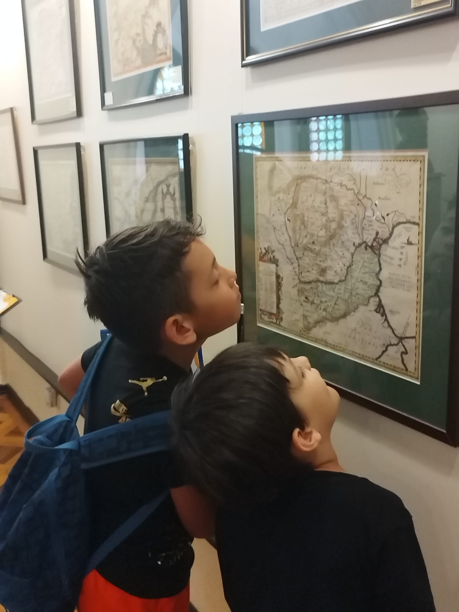 Two children closely examining a framed map on a museum wall.