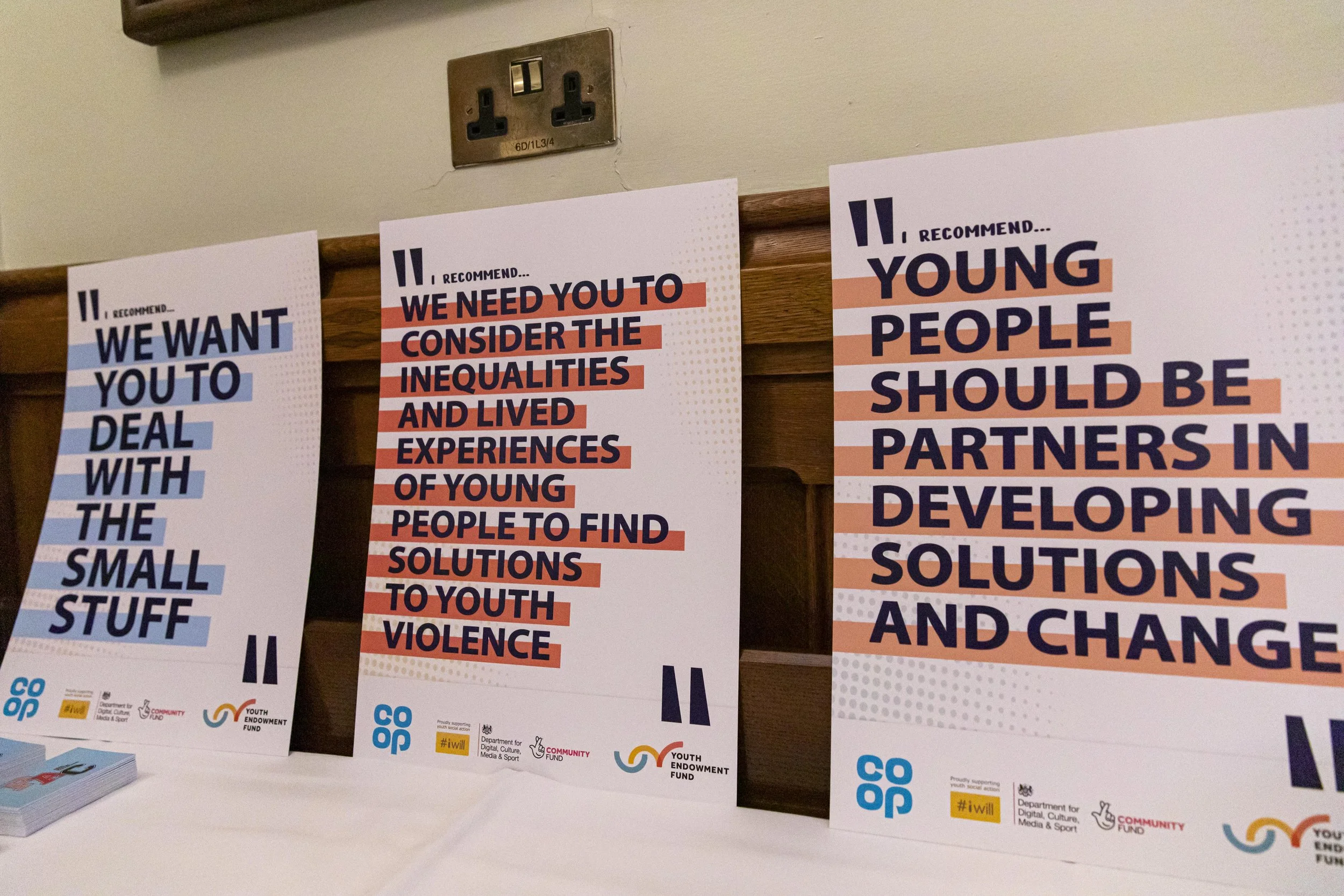 Posters with social messages promoting youth involvement, addressing inequalities, violence prevention, and collaborative development solutions, displayed on a table.