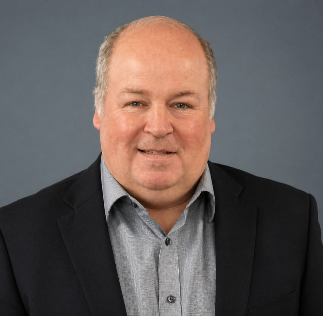 Jamie Saltzman wearing a dark blazer and a light button-up shirt, smiling against a neutral background.